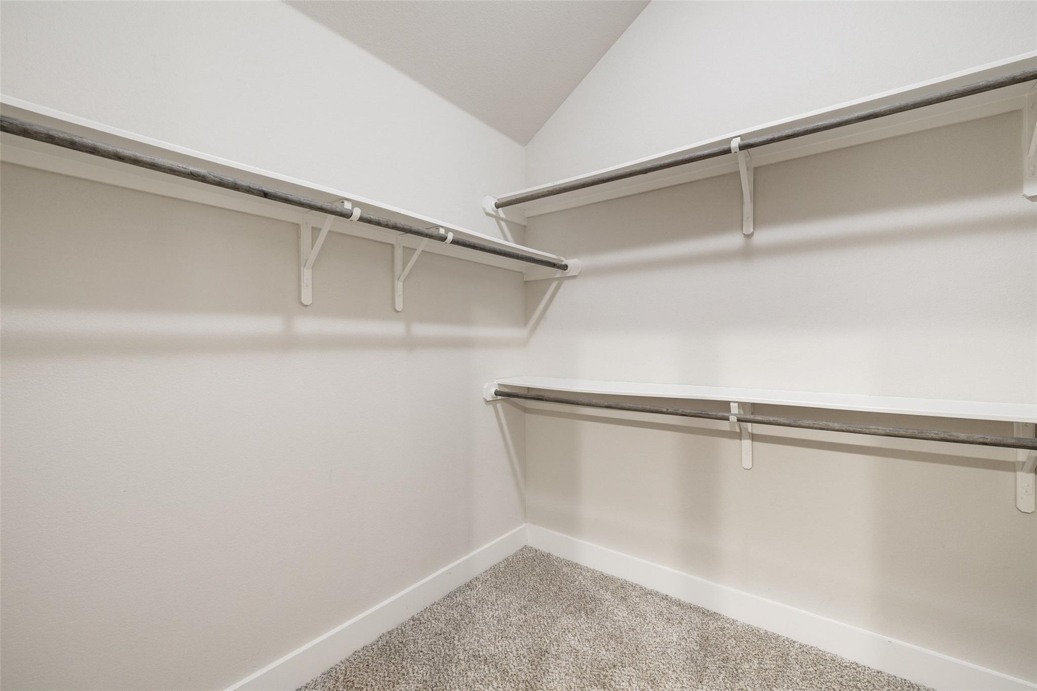 Empty walk-in closet with carpet flooring and clothes rods along two walls.