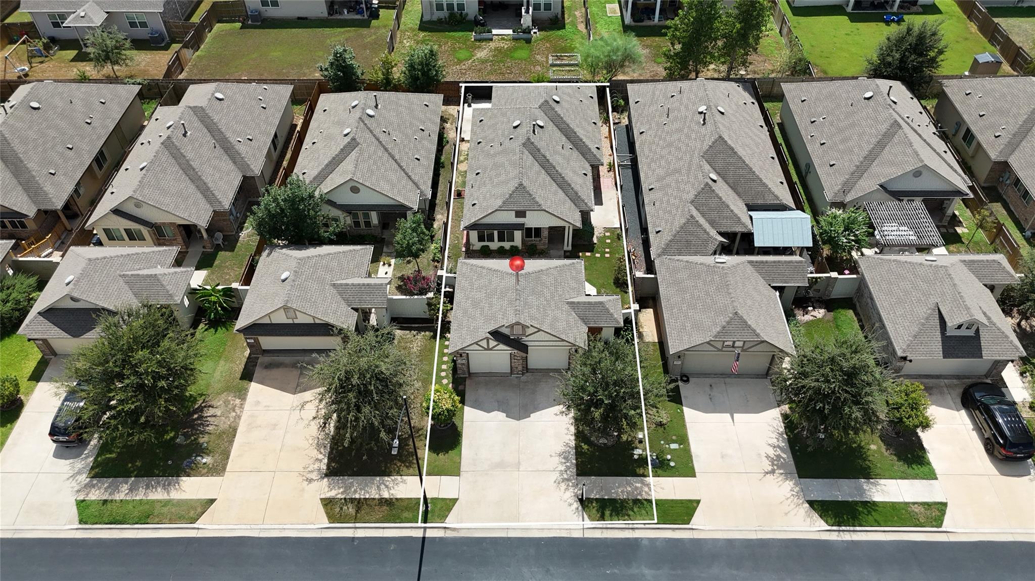 Aerial view of the outlined home, showing its roof, front yard, driveway, and neighboring houses.