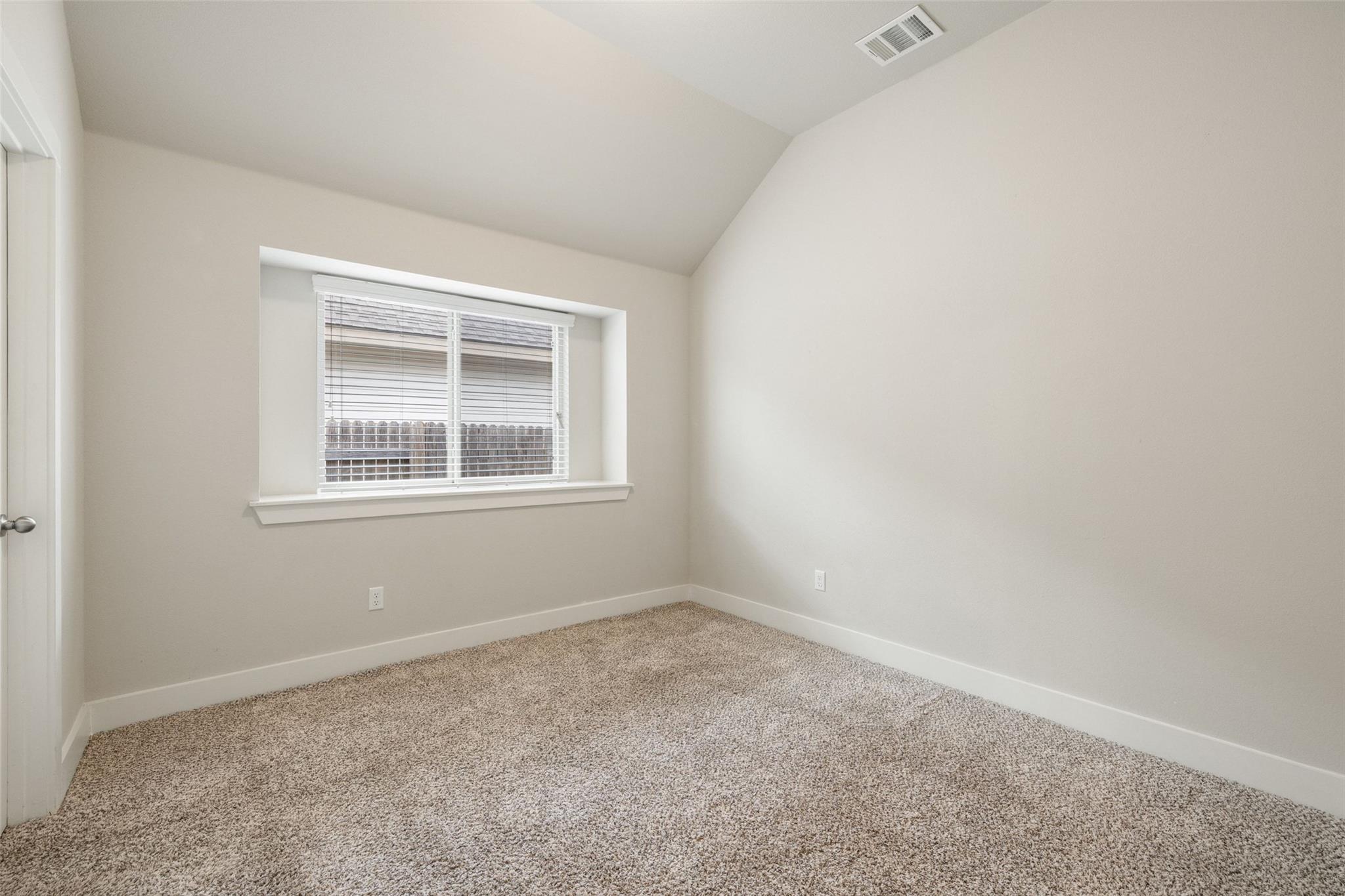 Empty bedroom with beige carpet, a sloped ceiling, and a window with white blinds.