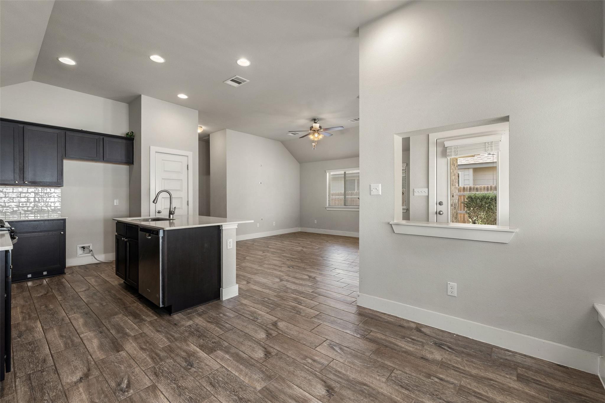 Open kitchen and living area with dark cabinetry, an island, and wood-look tile flooring.