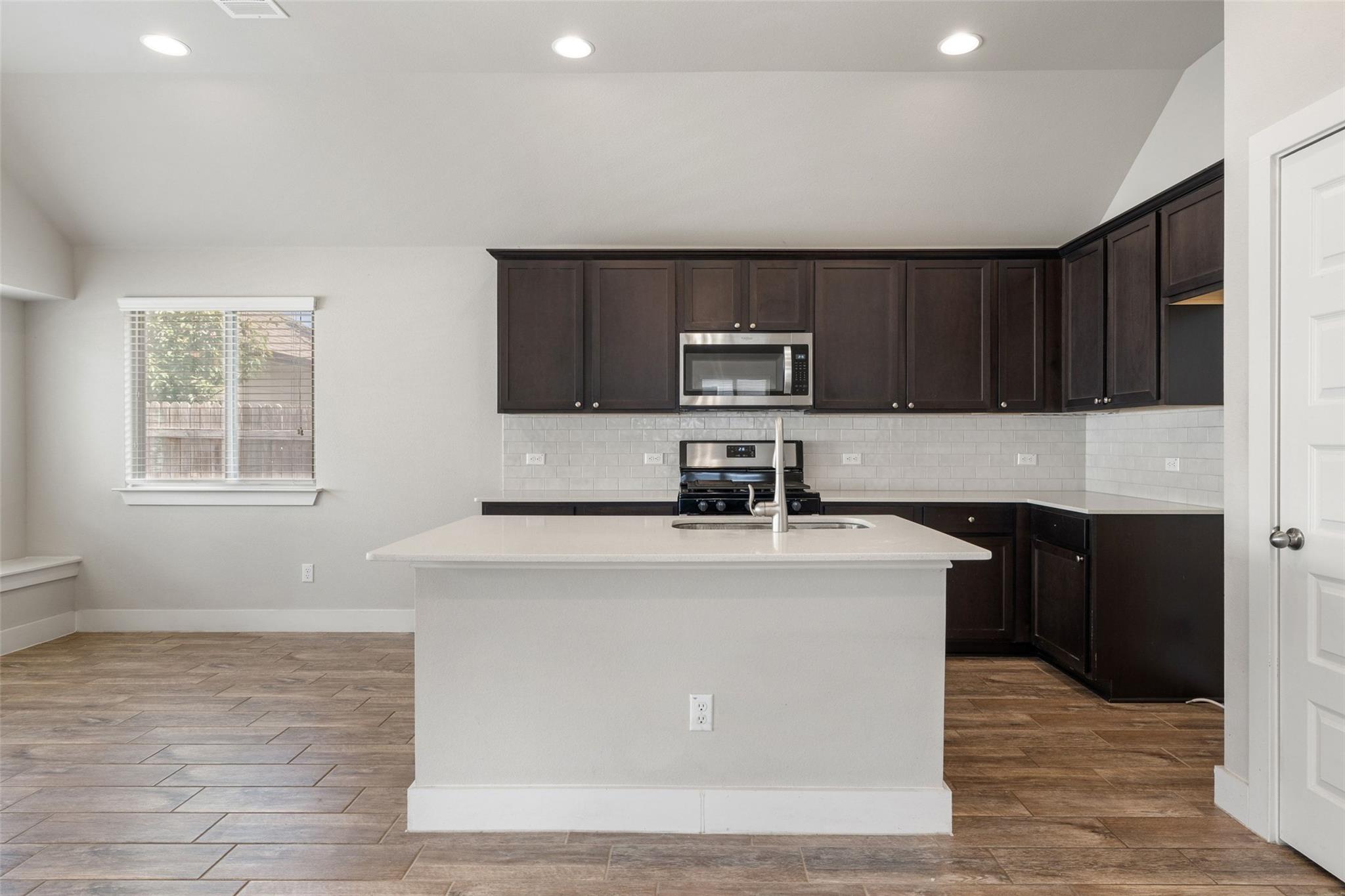 Kitchen with dark cabinets, a white island and subway tile backsplash, and brown tile flooring.