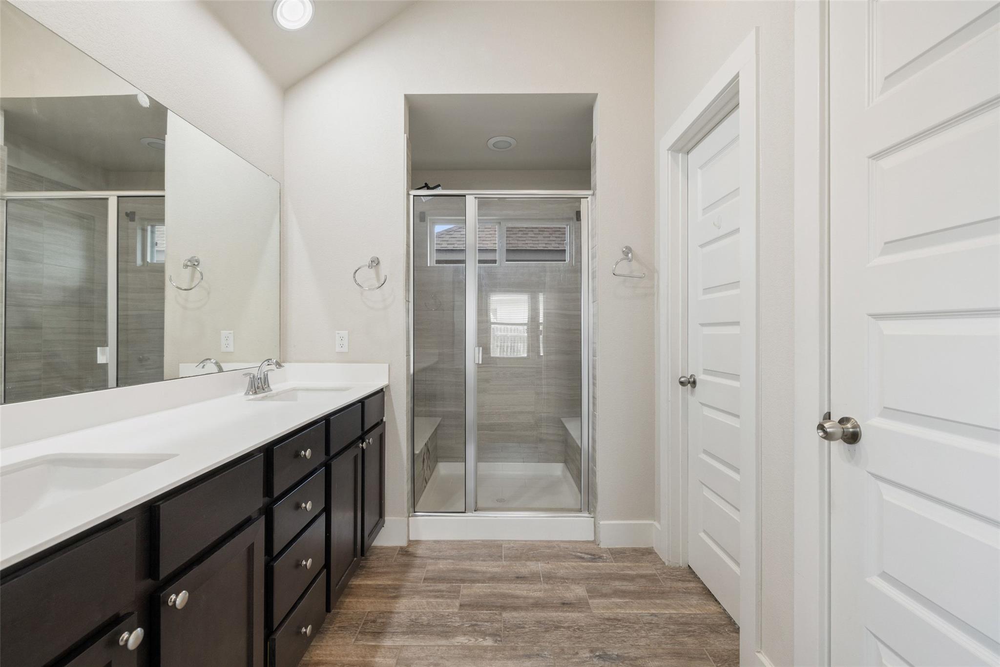 Bathroom with a dark double vanity and a glass-enclosed tiled shower.
