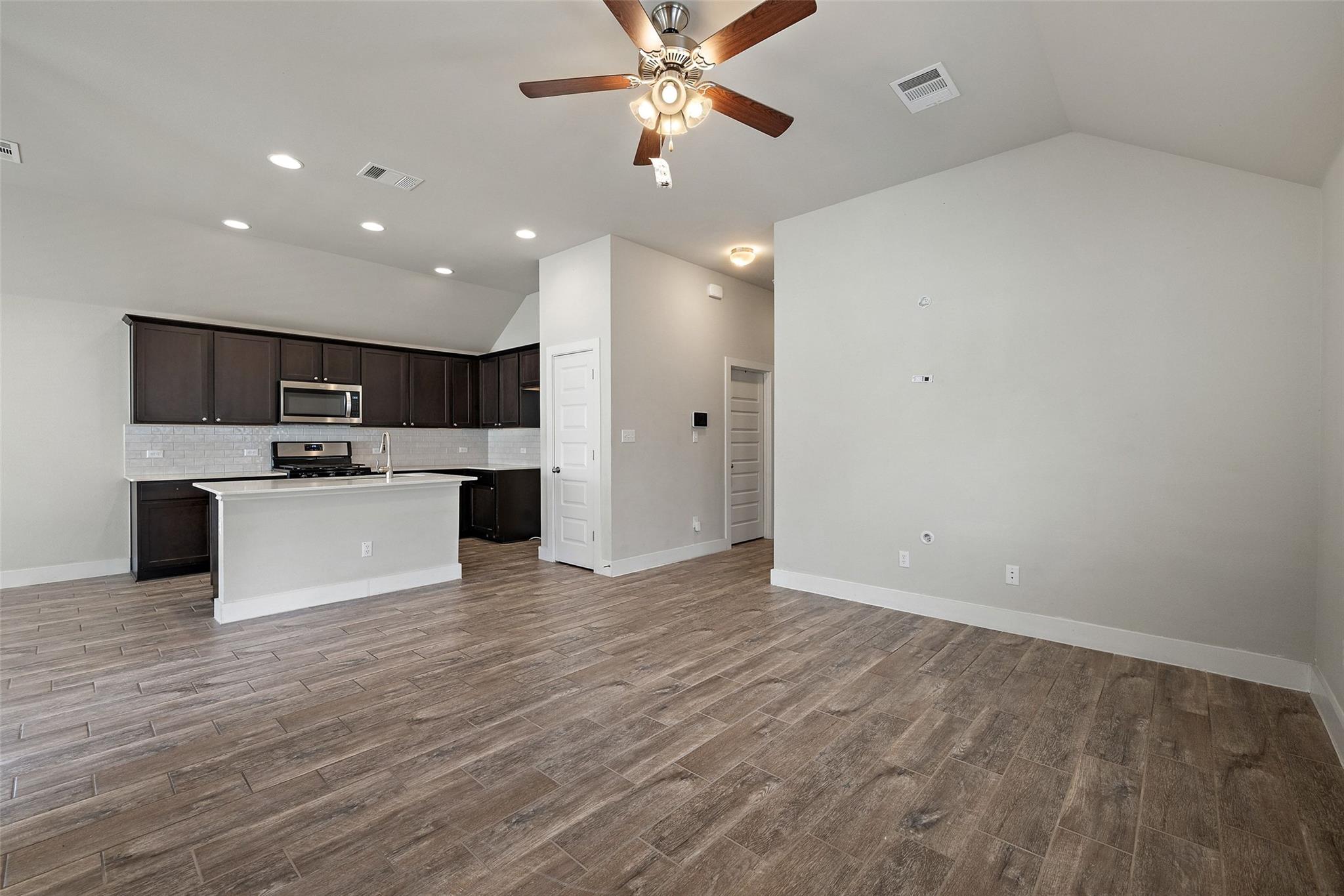Open-plan kitchen with dark cabinets, a white island, and wood-look tile flooring.