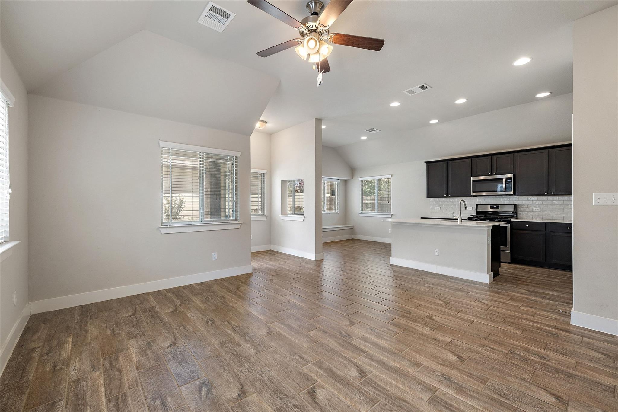 Open-plan kitchen and living area with dark cabinets, a central island, and wood-look tile floors.