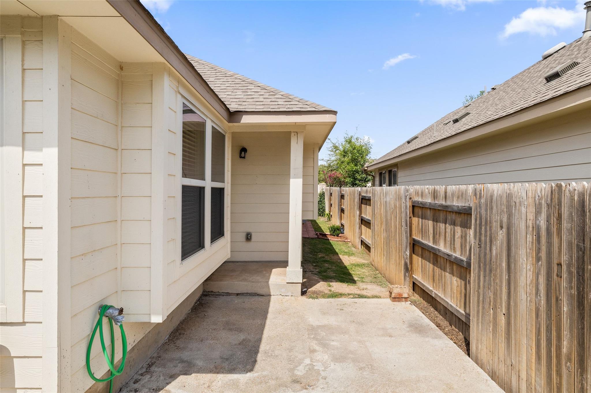 Side patio beside a light-colored home, bordered by a tall wooden privacy fence.