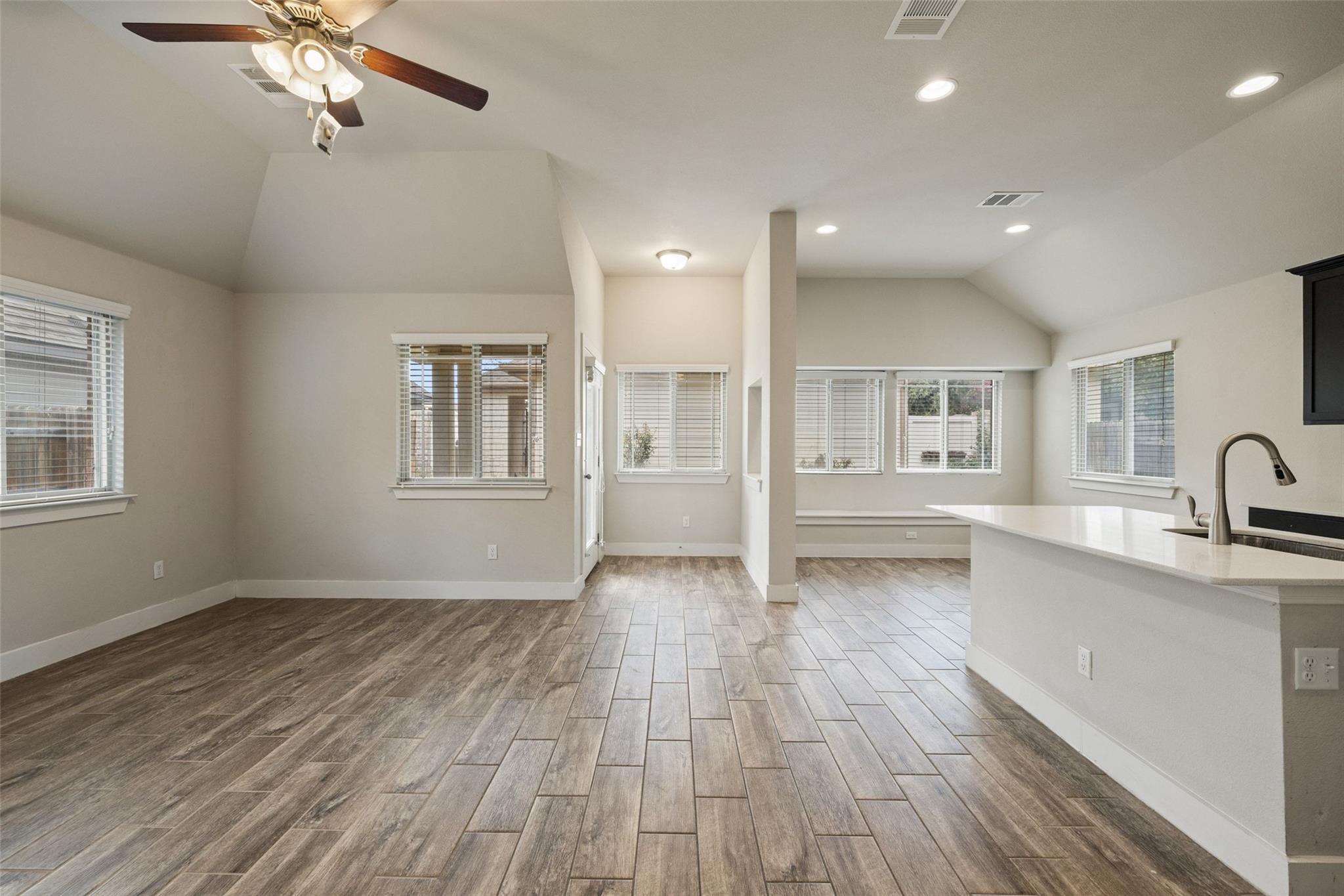 Open-plan living area with wood-look tile floors, vaulted ceiling, and kitchen peninsula.