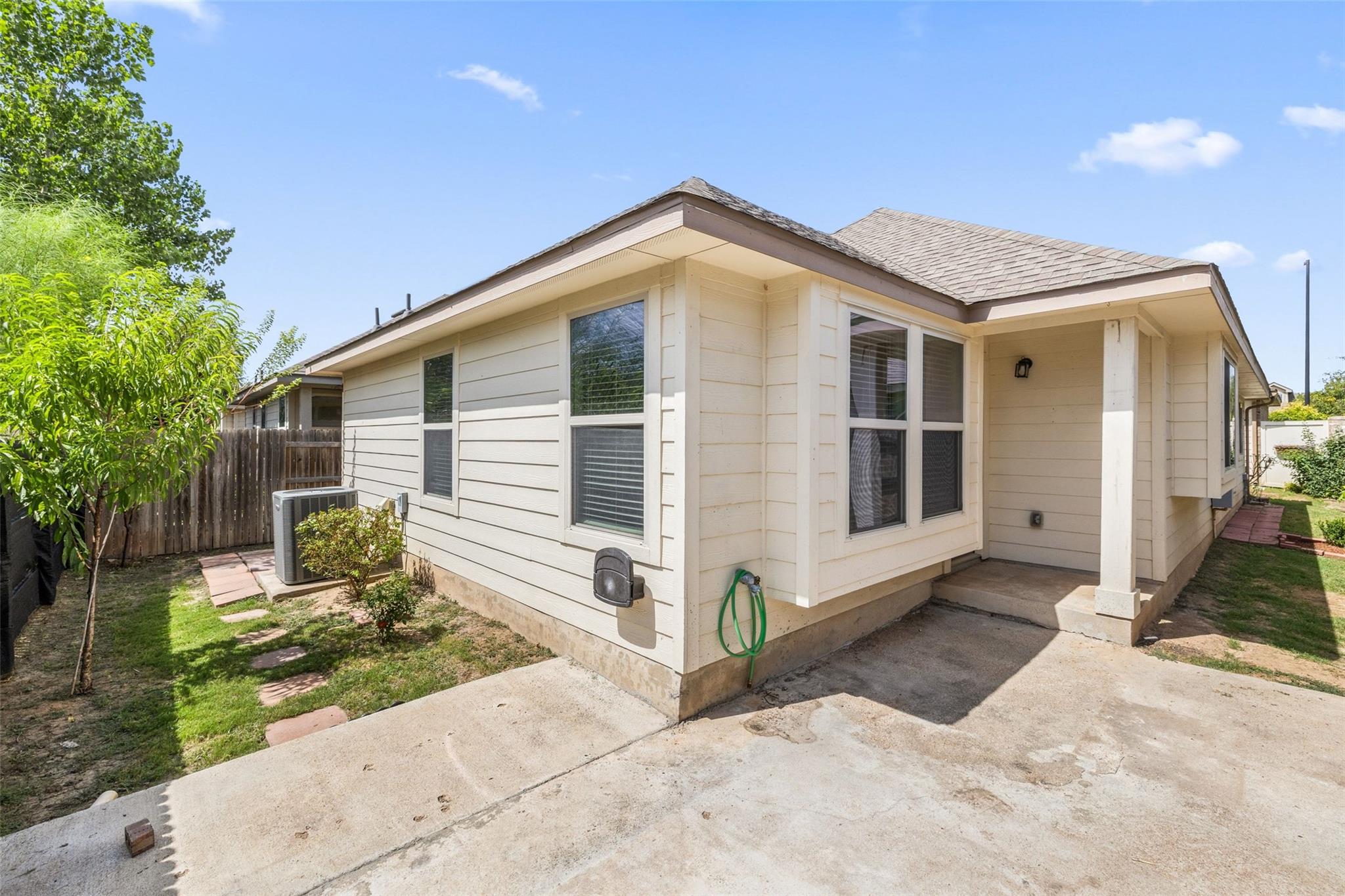 Cream-colored home exterior with a covered patio, concrete slab, and narrow fenced lawn.