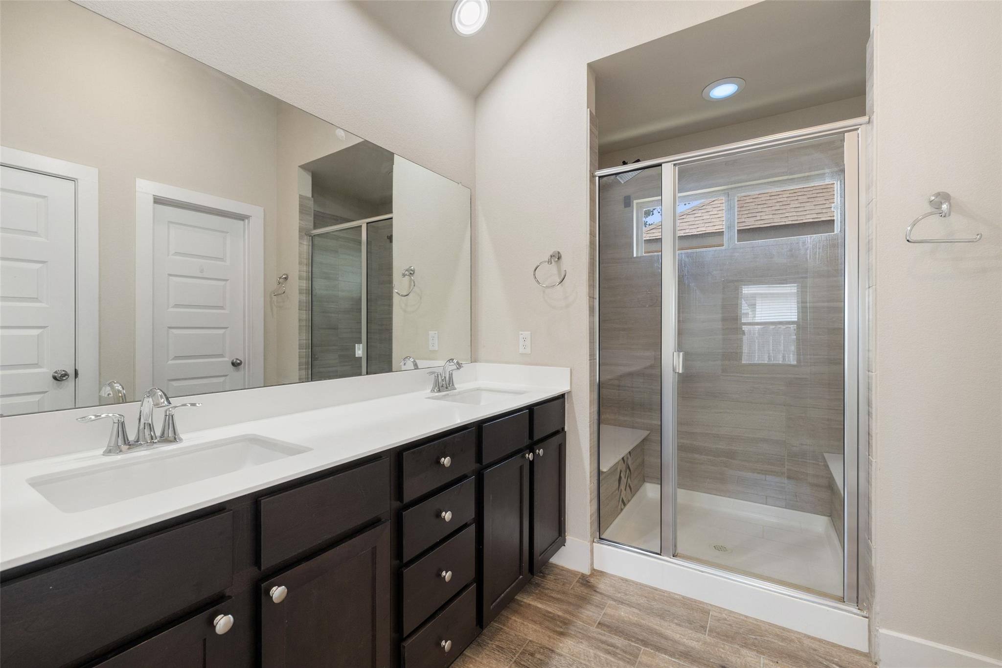 Bathroom with a double-sink vanity and glass-enclosed tiled shower.