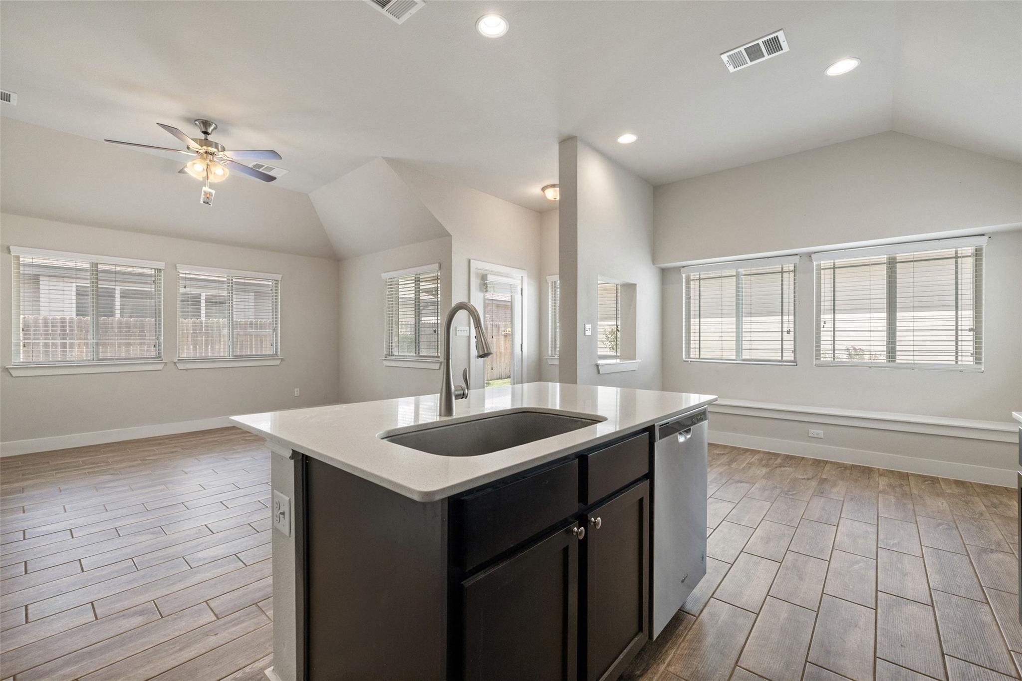 Vacant kitchen with a dark island, white countertop, large windows, and light wood-look tile flooring.