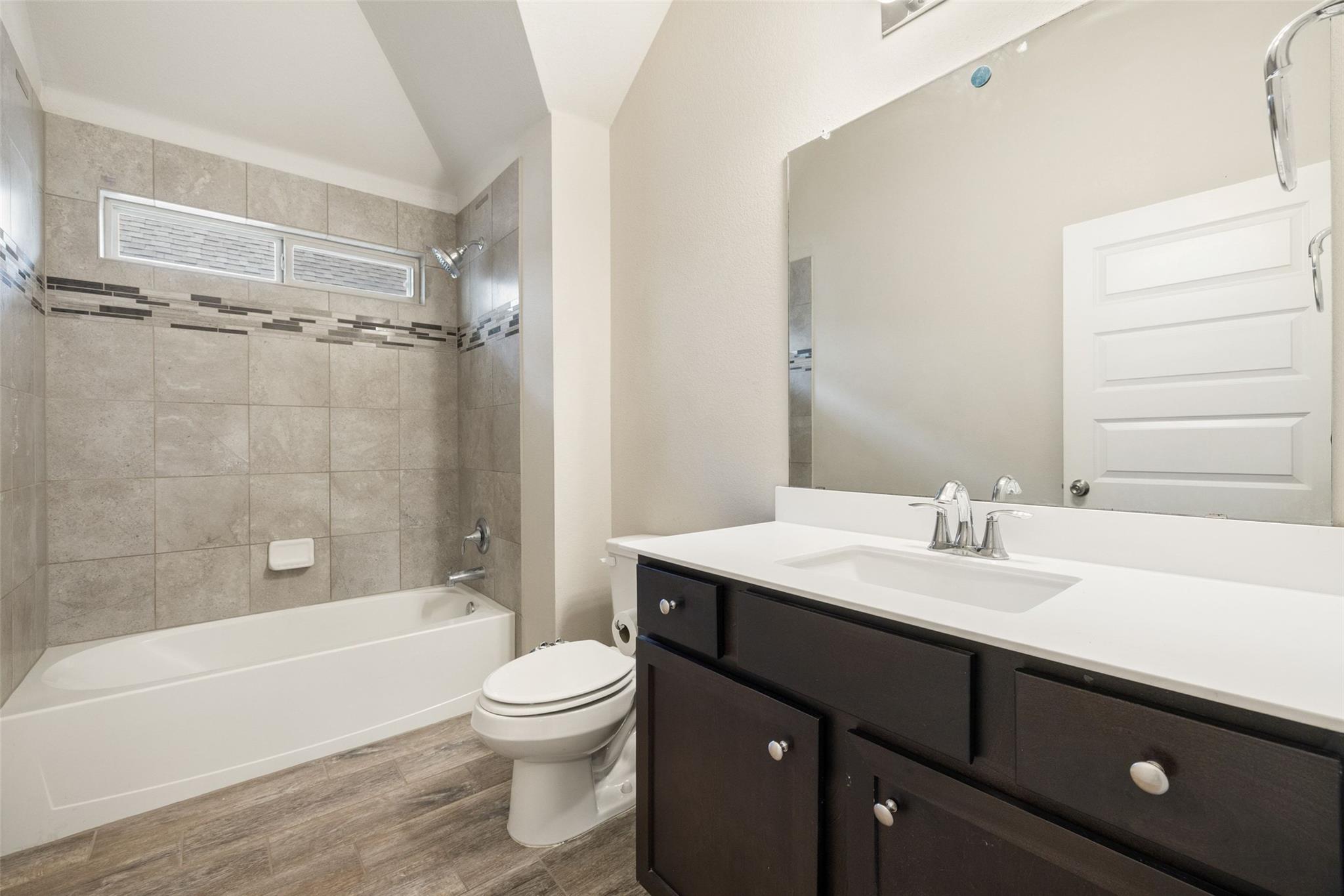Bathroom with a tiled tub and shower, dark vanity, white countertop, and large mirror.