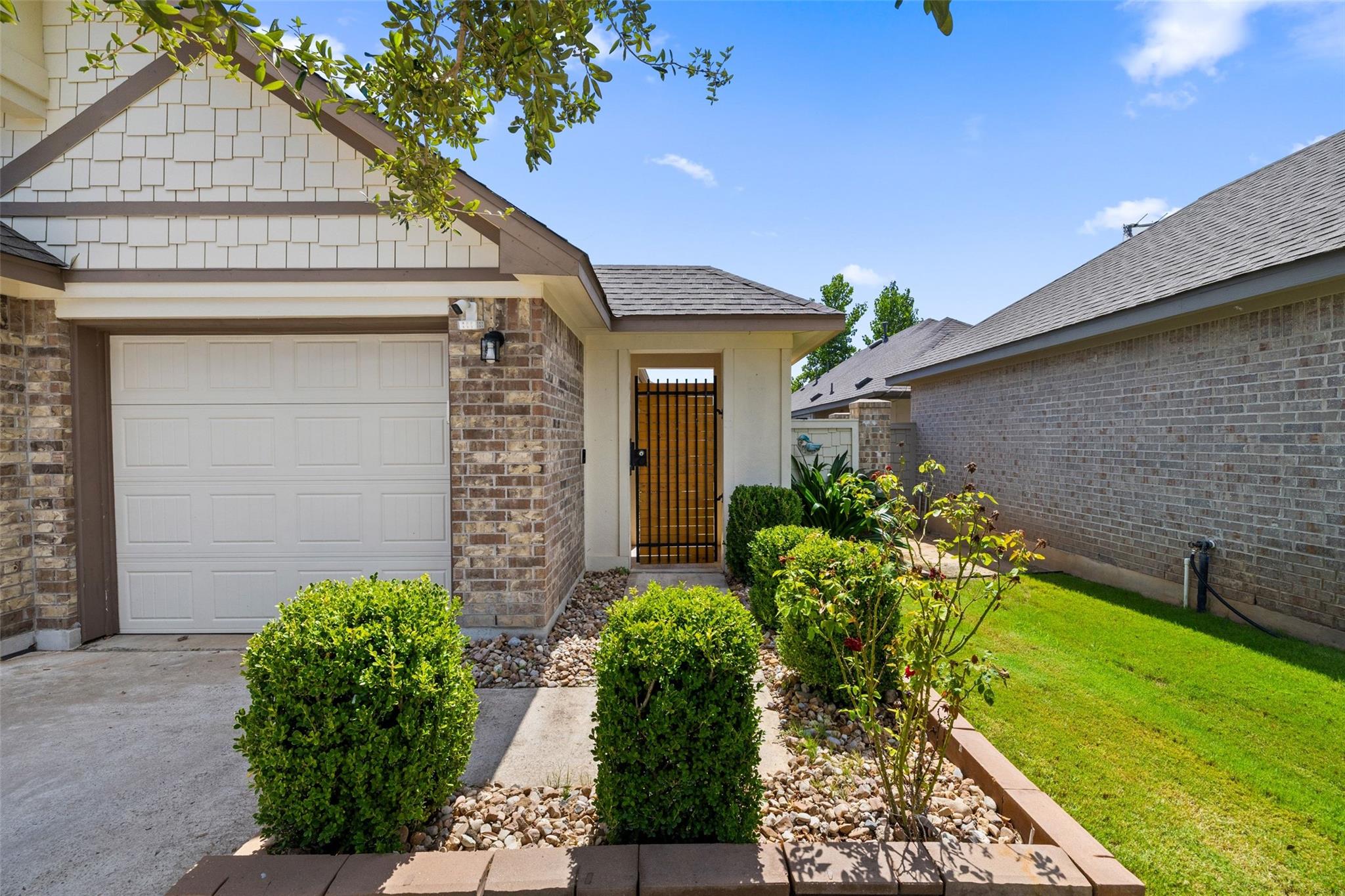 Home exterior with a paneled garage, gated entry, landscaped shrubs, and a small lawn.