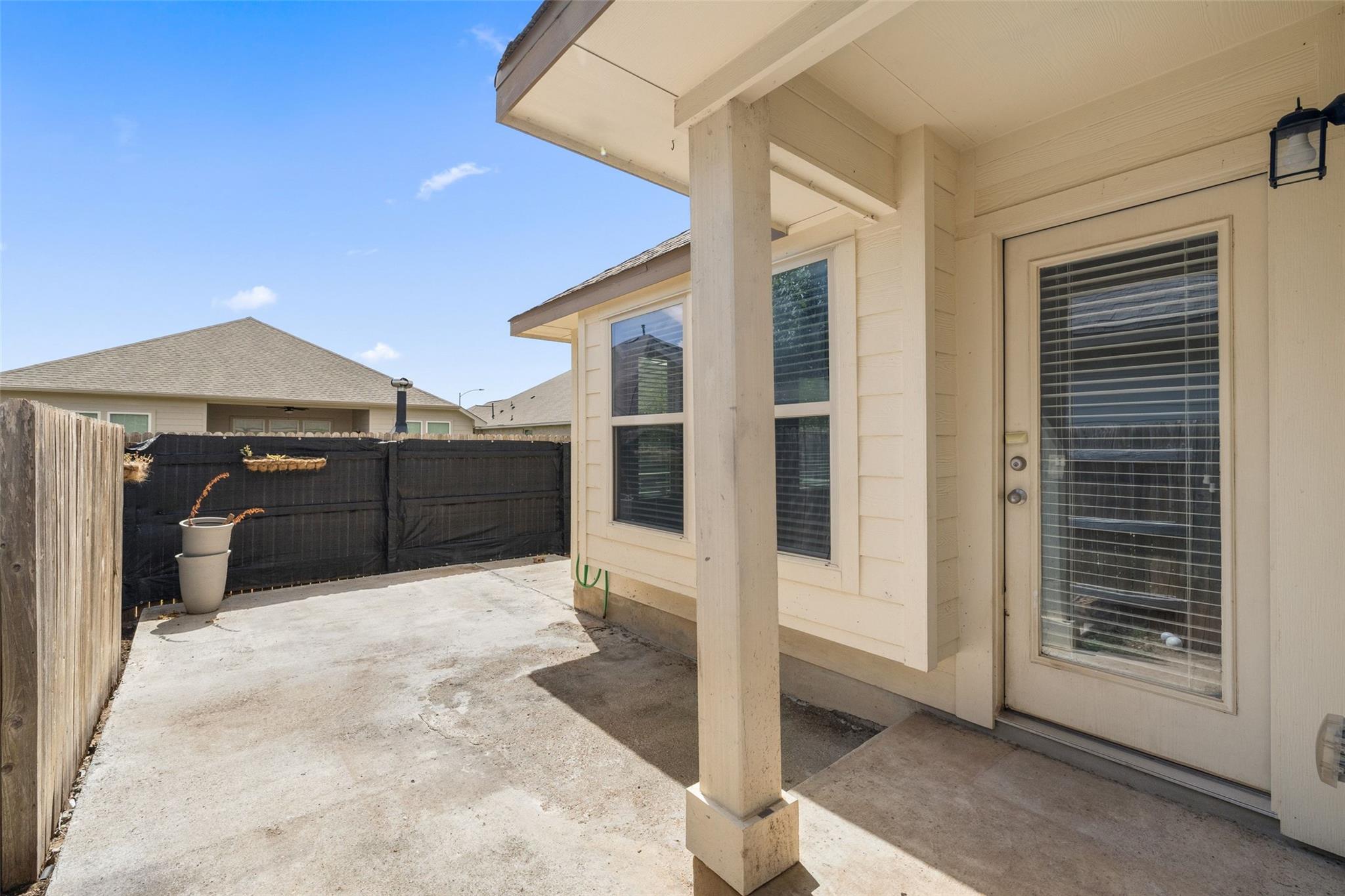 Covered concrete patio beside the home's rear glass door, enclosed by privacy fencing.