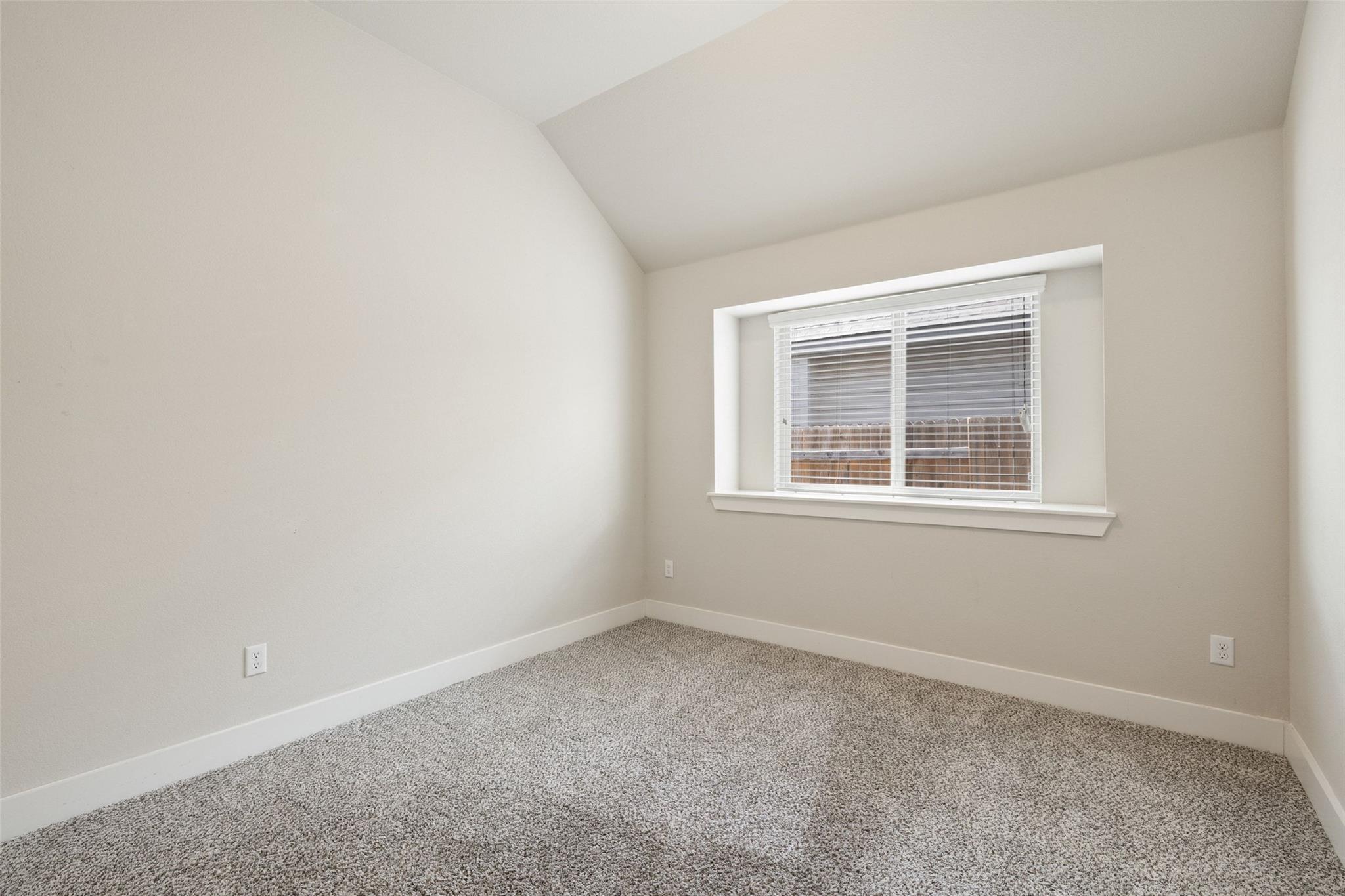 Empty bedroom with gray patterned carpet, a sloped ceiling, and a window with white blinds.