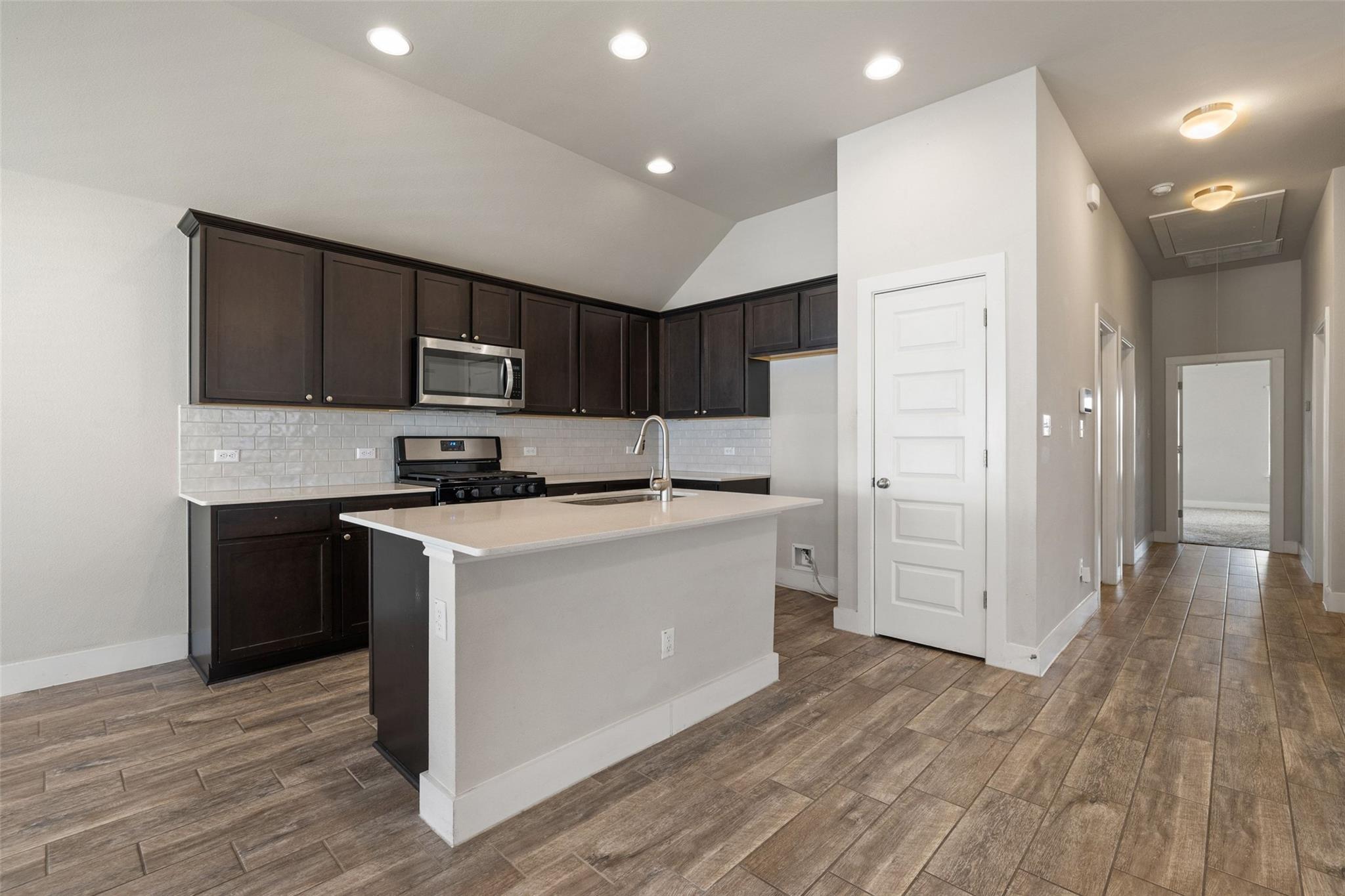 Kitchen with dark cabinets, stainless steel appliances, a white island, and wood-look tile floors.