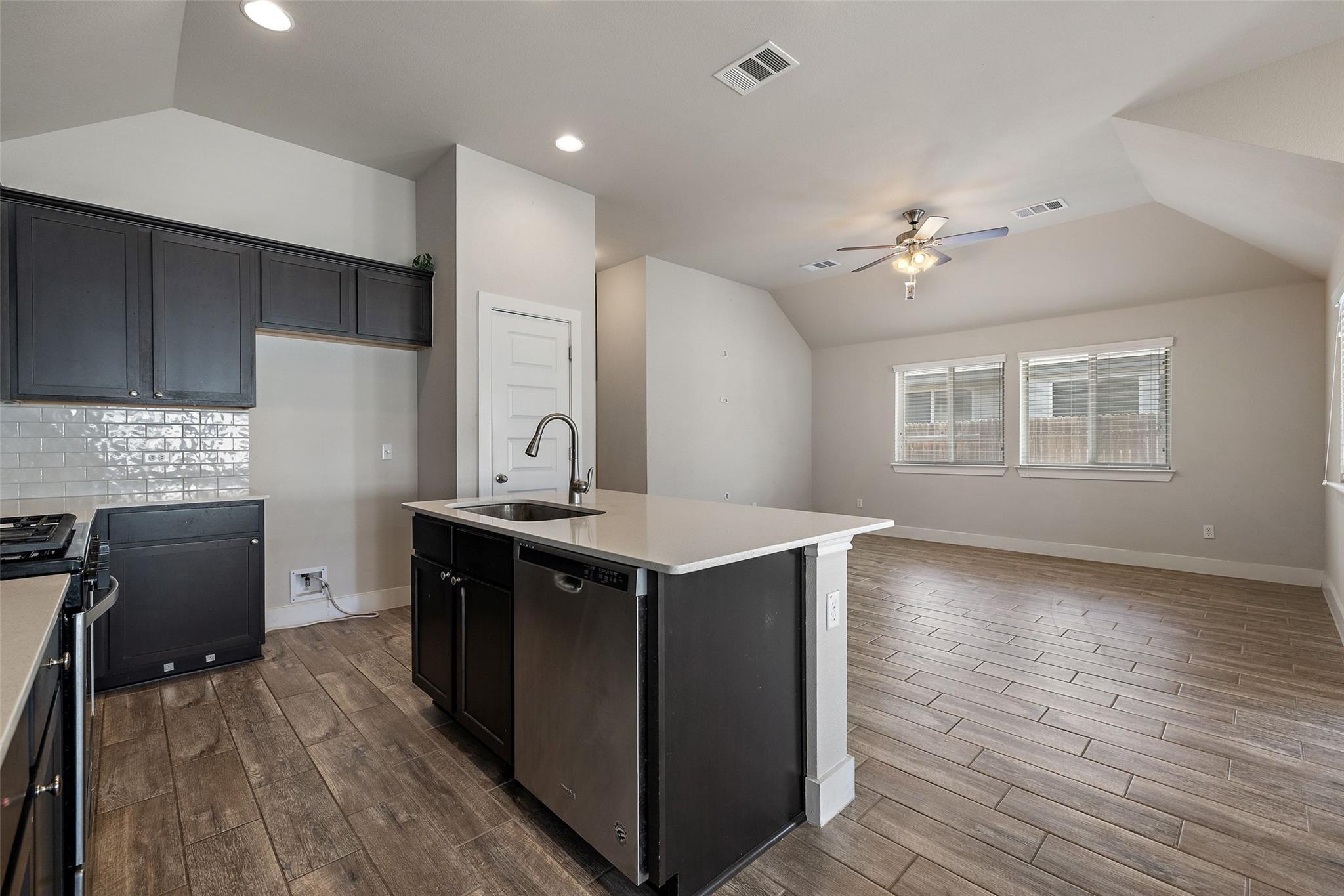 Kitchen with dark cabinets and a large island opening into an unfurnished living area.
