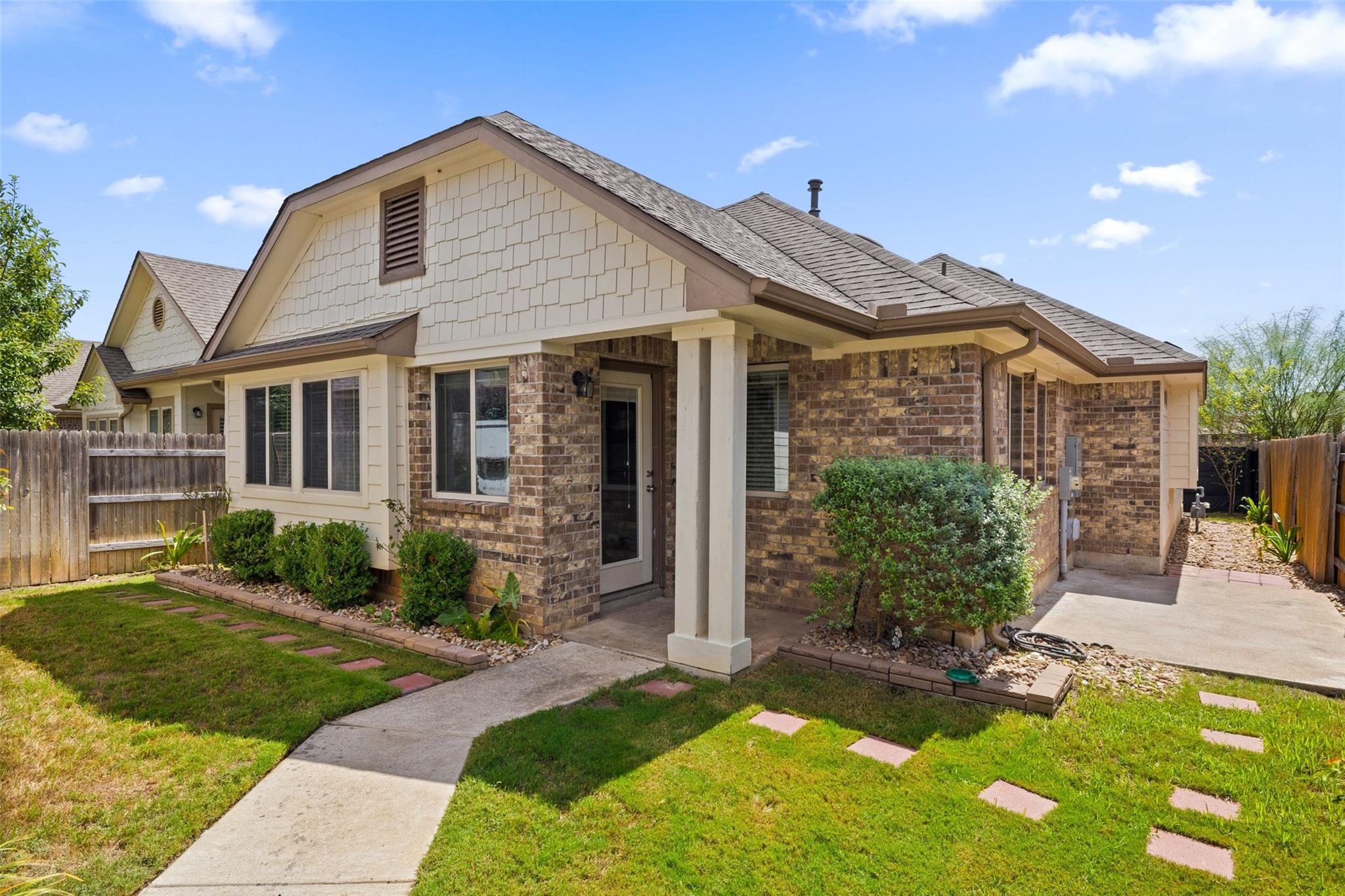 Single-story brick-and-shingle home with a covered entrance, lawn, and stepping-stone path.