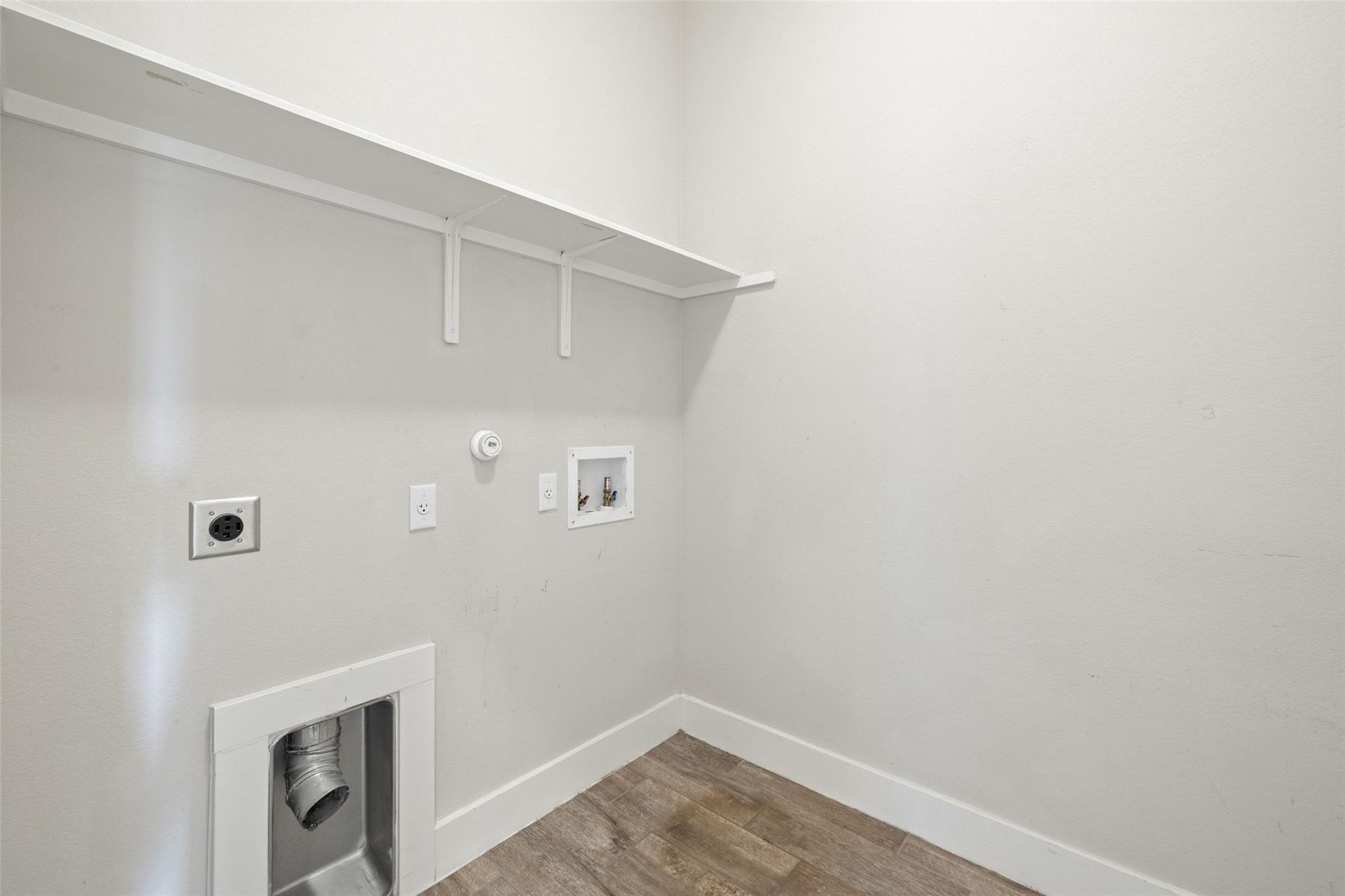 Empty laundry closet with a long shelf, washer hookups, and a dryer vent.