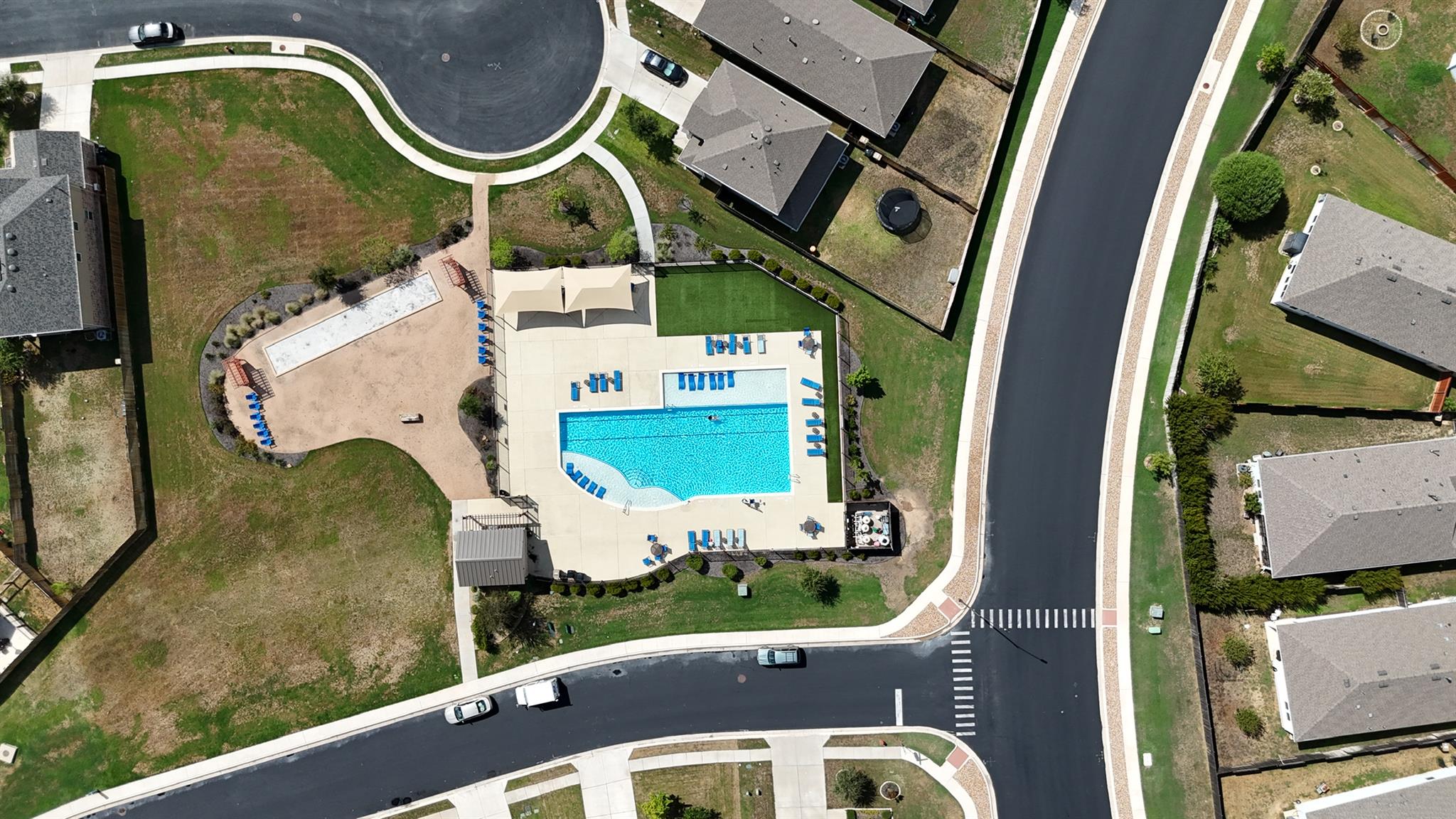Aerial view of a neighborhood pool with shade canopies and lounge chairs, surrounded by homes and streets.