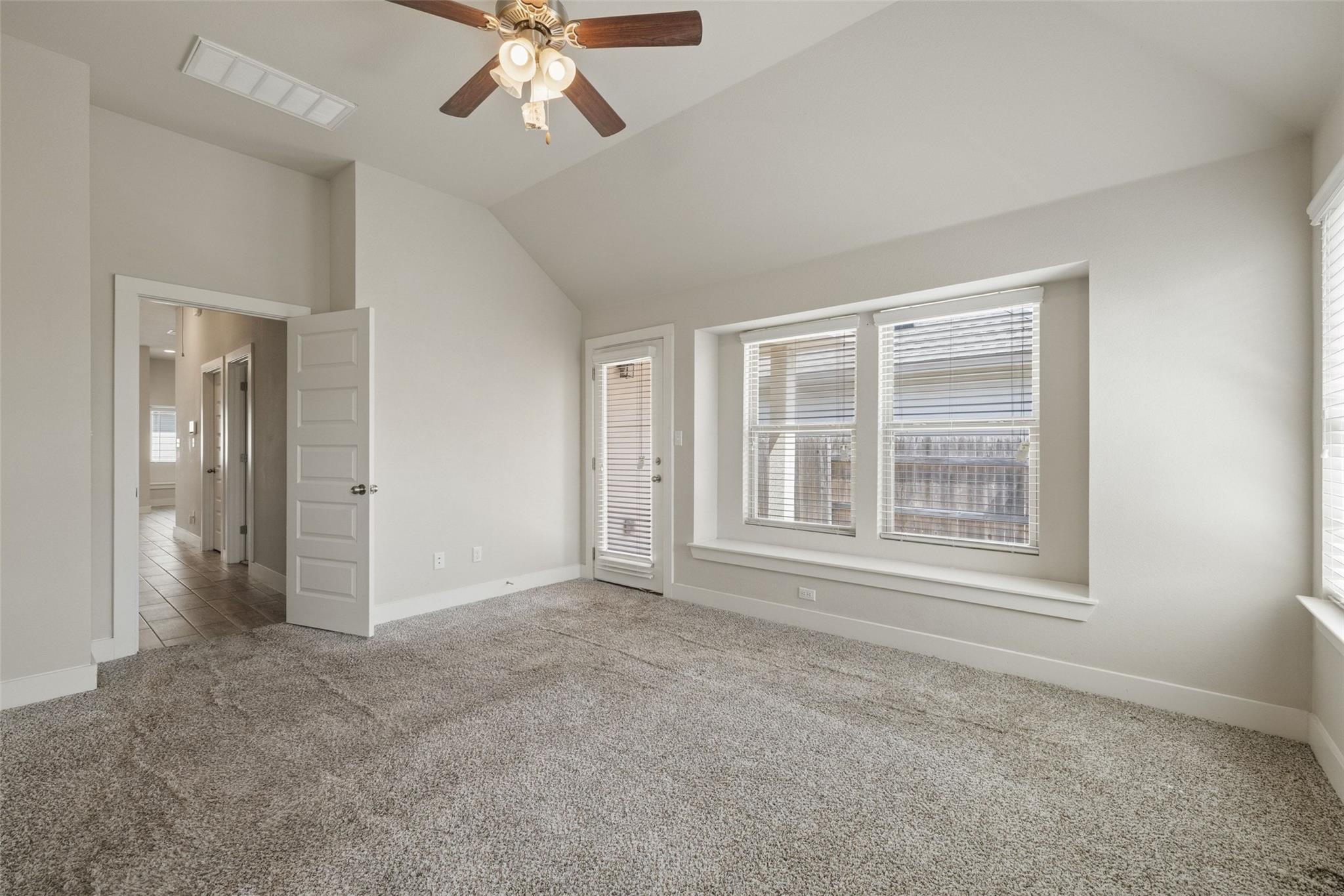 Empty carpeted bedroom with a vaulted ceiling, ceiling fan, and wide windows with blinds.