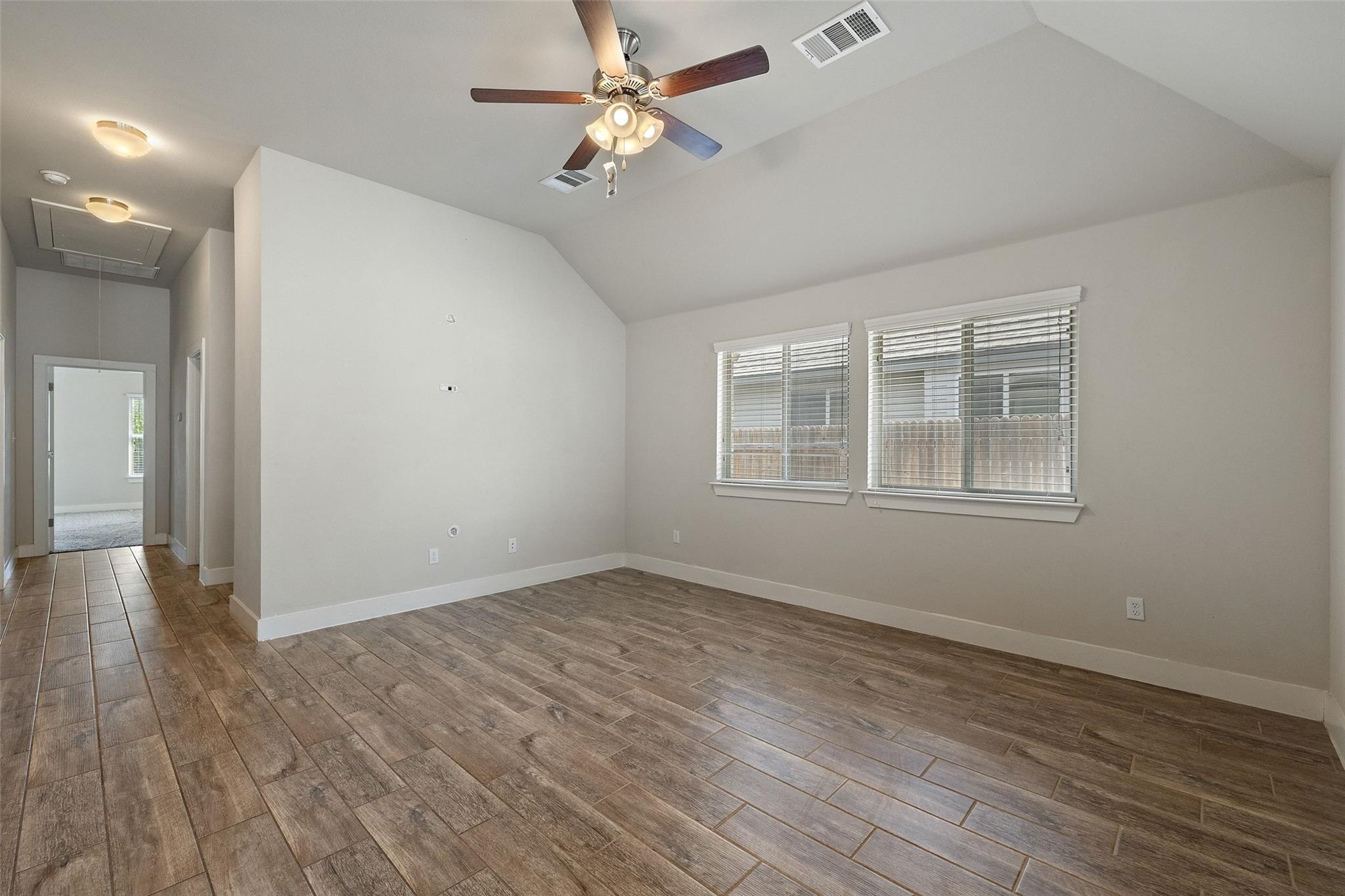 Empty living room with a vaulted ceiling, ceiling fan, and wood-look tile flooring.