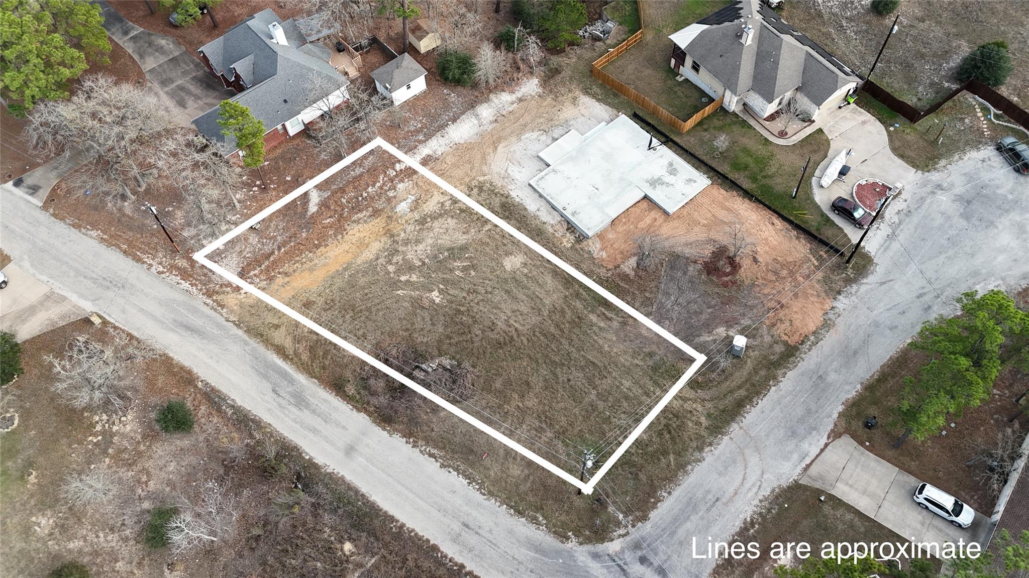 Aerial view of an undeveloped corner lot outlined in white beside neighboring homes.