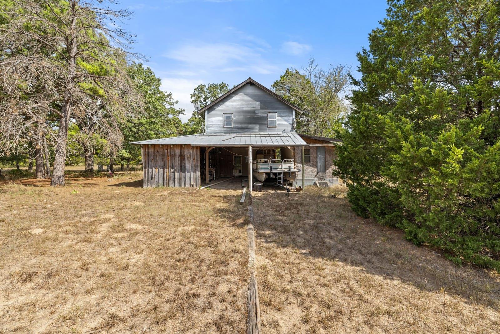 Two-story gray house with a broad covered patio and mature trees around a dry yard.