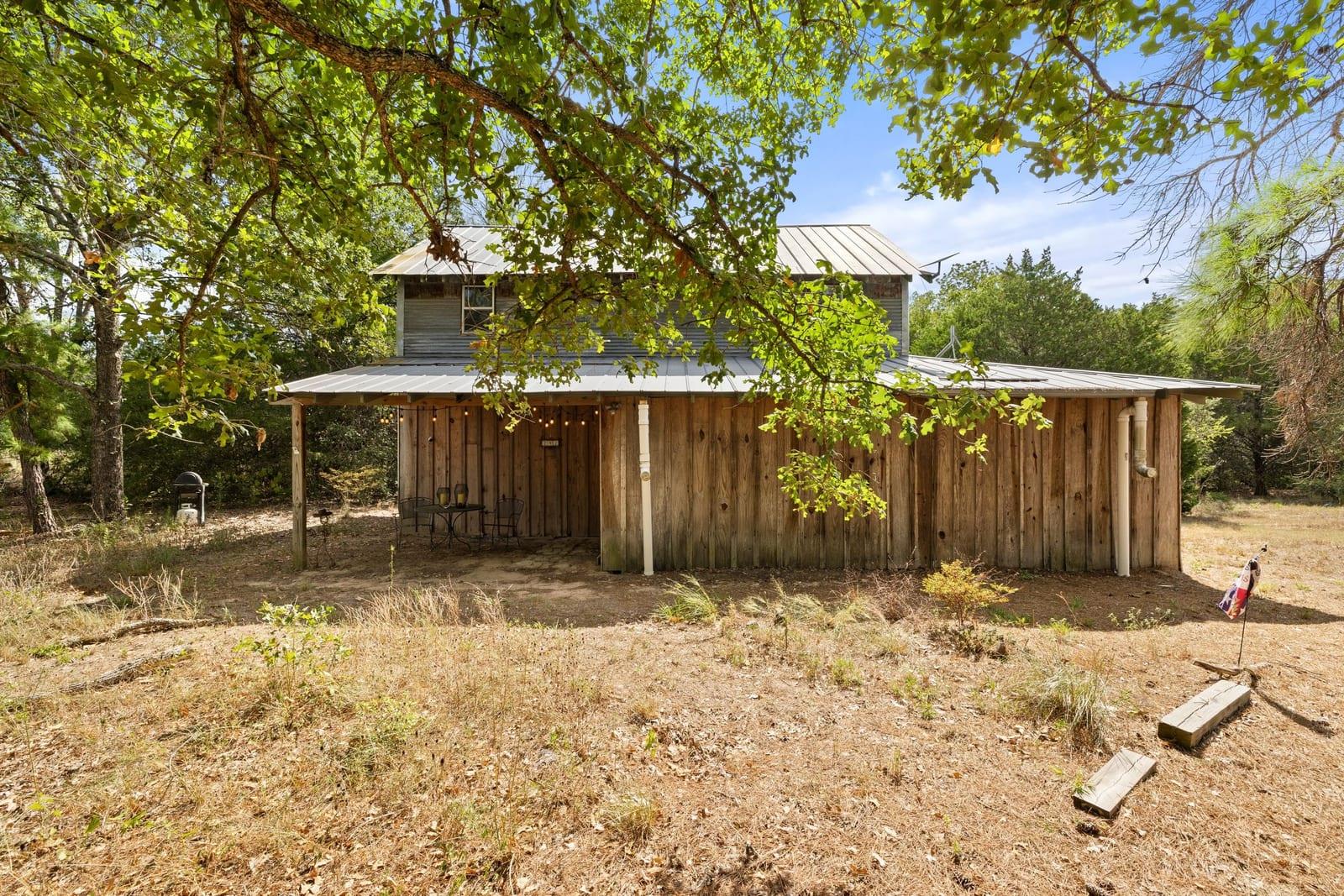 Wood-sided home with a metal roof and covered patio beneath mature trees.
