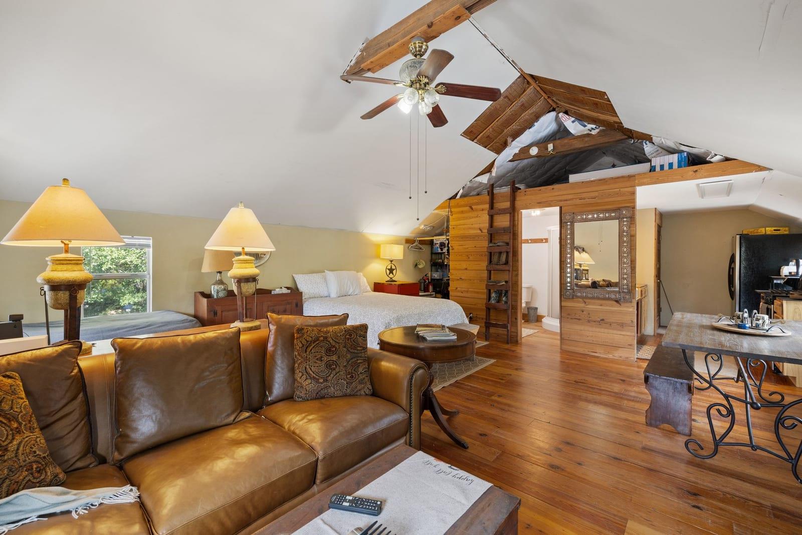 Open-plan living and sleeping area with a leather sofa and exposed timber rafters above the bed.