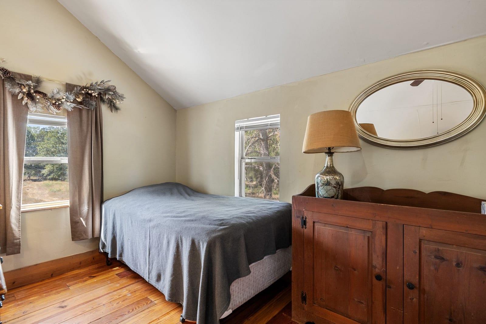 Bedroom with a gray-covered bed, sloped ceiling, hardwood floors, and rustic wooden dresser.