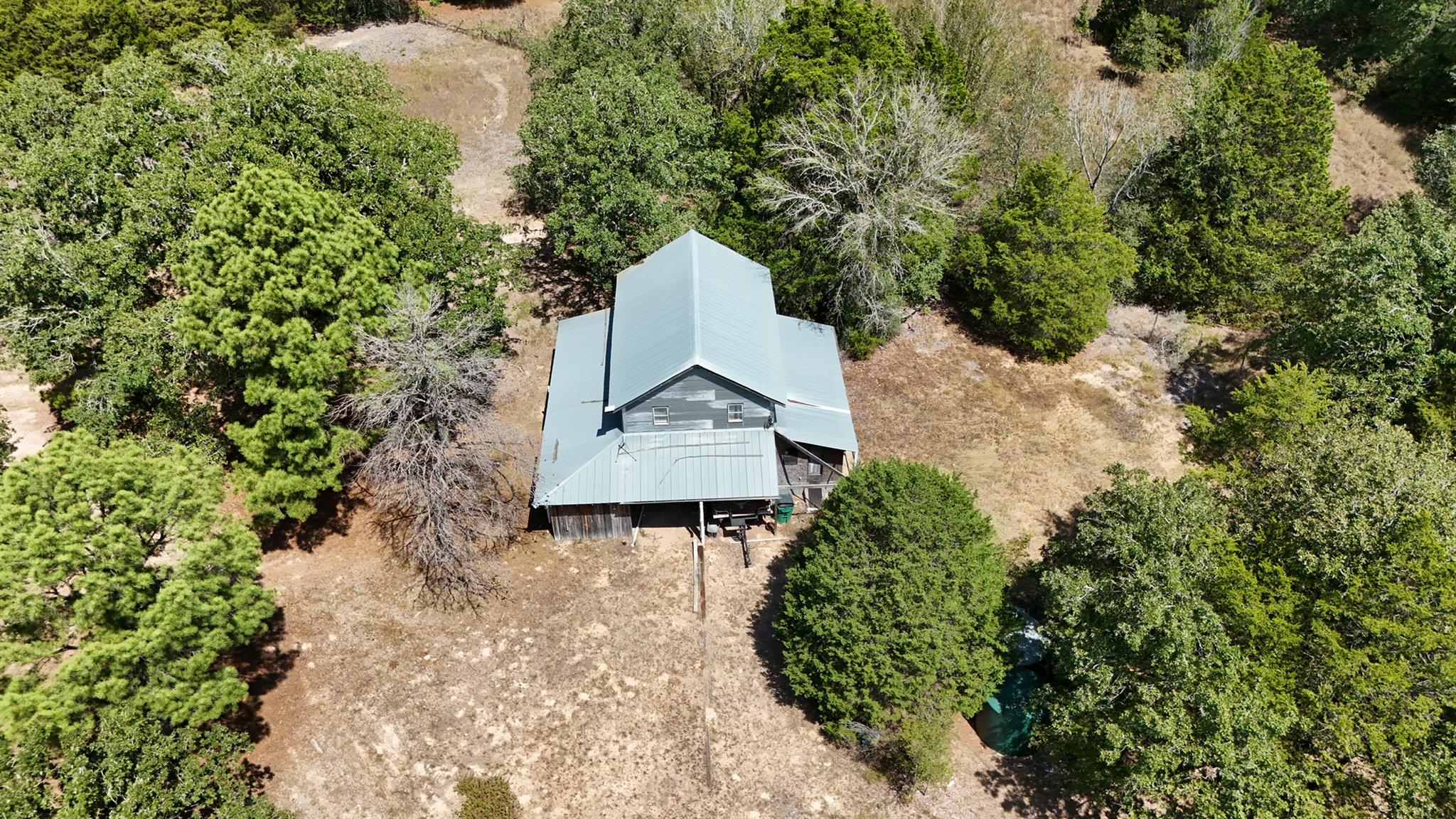 Aerial view of a metal-roofed house among trees, with a partially visible swimming pool.