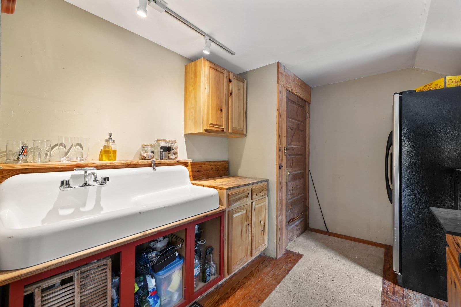 Utility room with a large white sink, red vanity, wood cabinets, and black refrigerator.