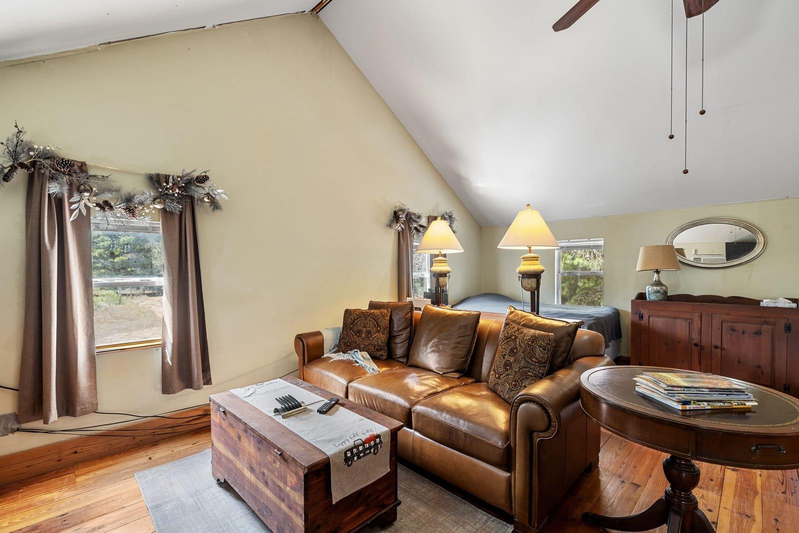 Living room with a vaulted ceiling, leather sofa, and hardwood floors.