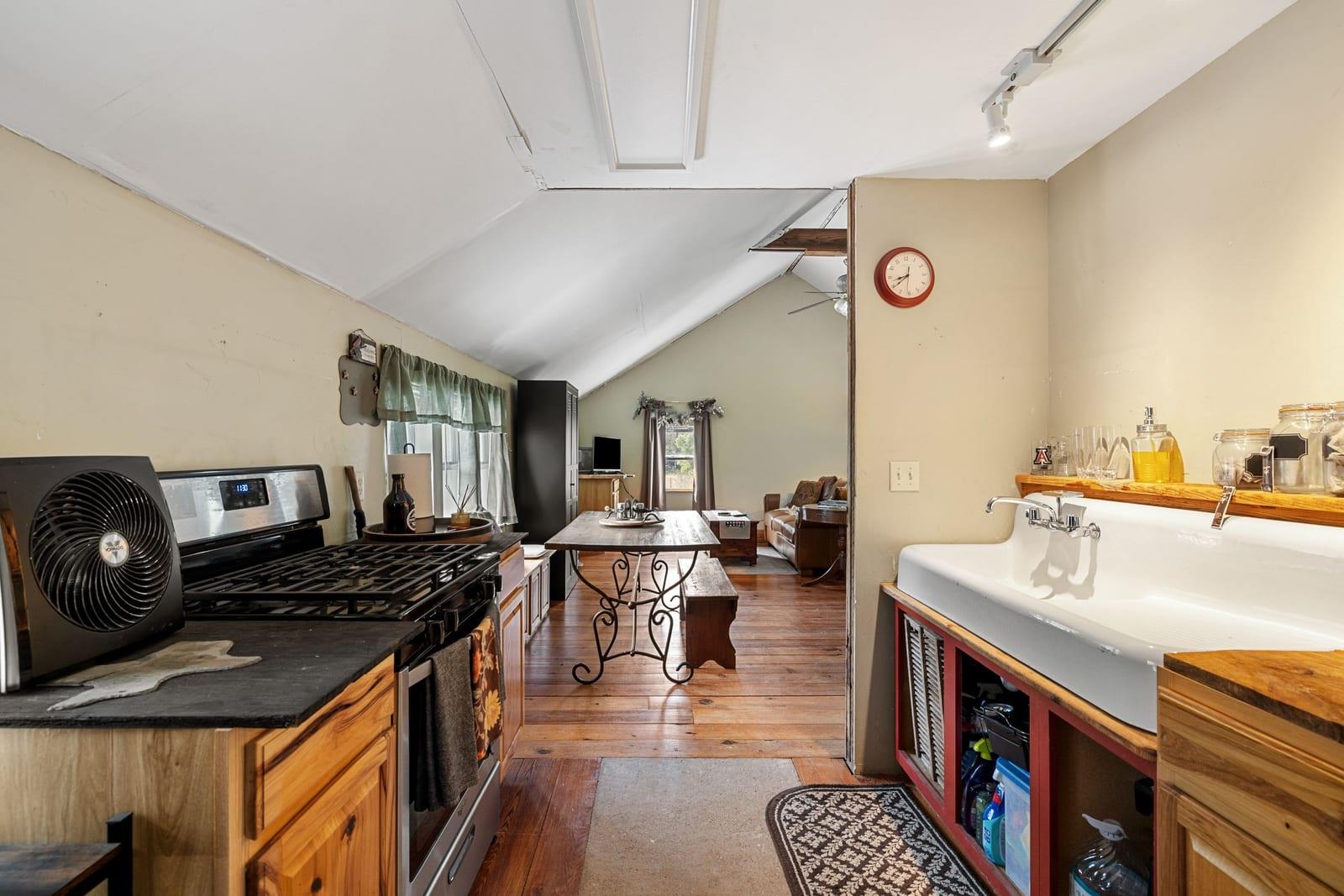Kitchen with wood cabinetry and black range opening into a living area beneath a vaulted ceiling.