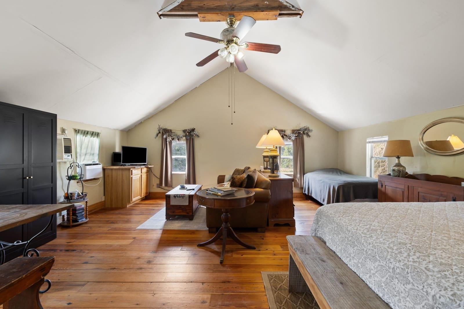 Furnished bedroom with a vaulted ceiling, ceiling fan, and polished wood floors.