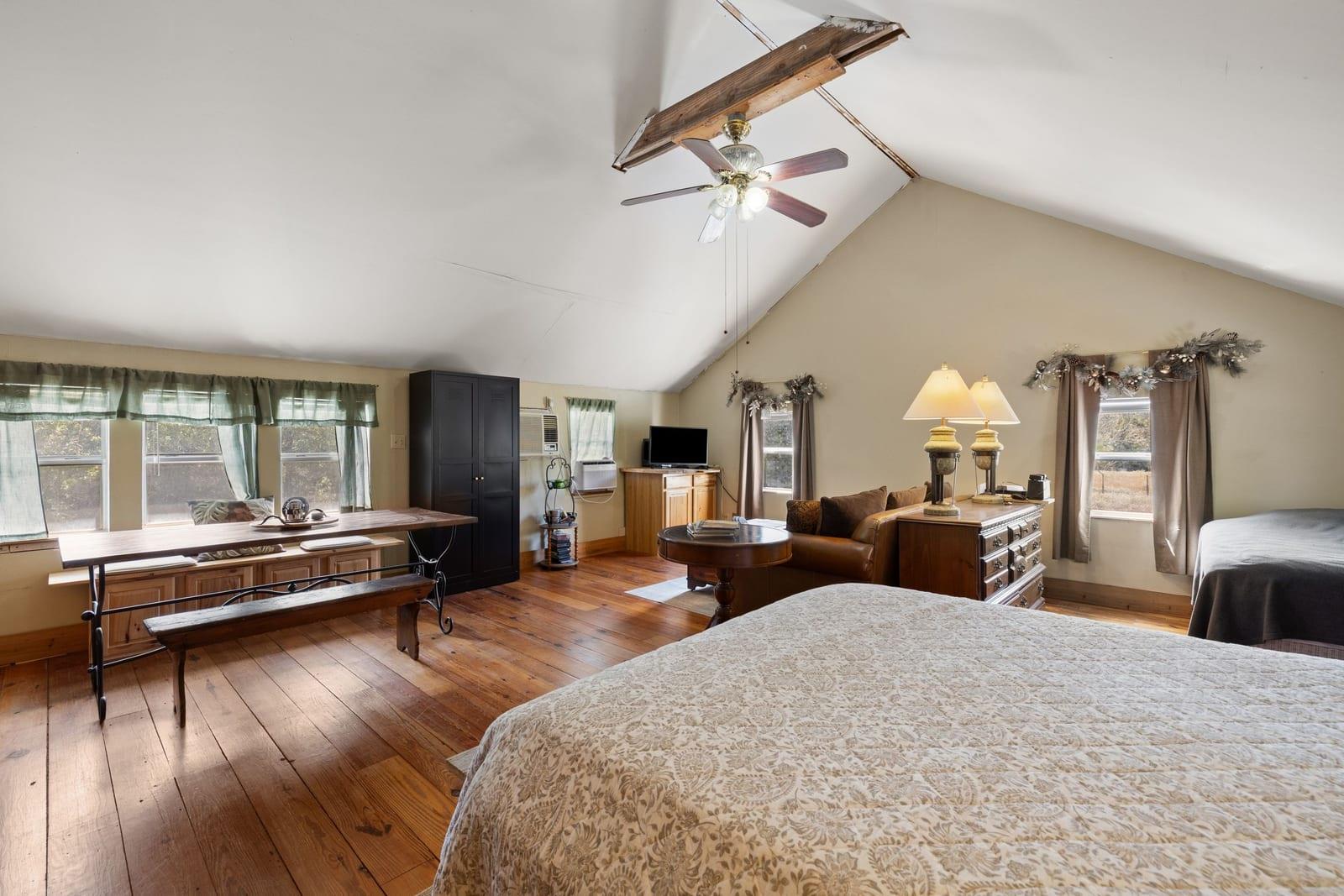Furnished bedroom with a vaulted ceiling, exposed beam, and hardwood floors.