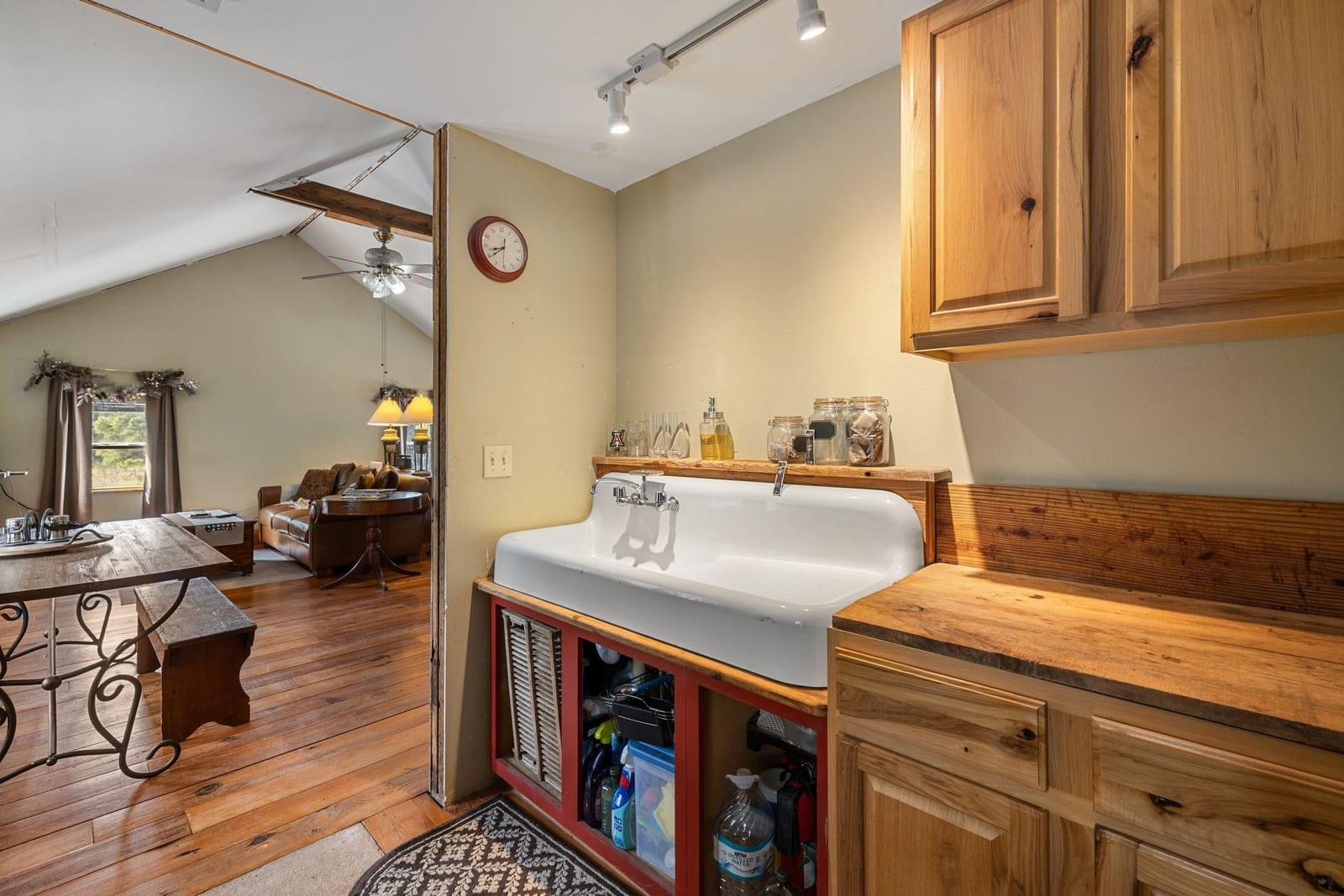 Large white sink in rustic wood cabinetry, with an adjoining living area under a vaulted ceiling.