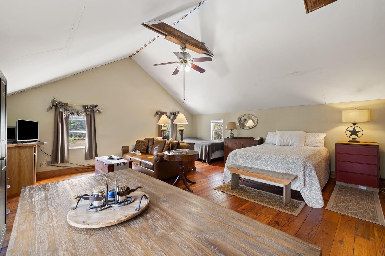 Furnished bedroom with a vaulted ceiling, hardwood floors, a large bed, and a leather sitting area.