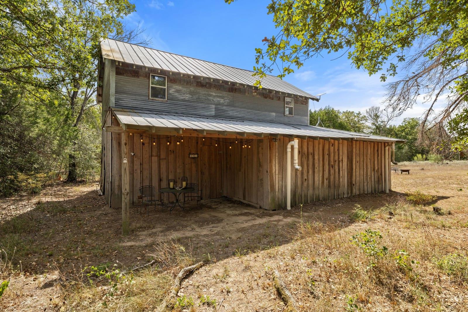 Rustic two-story wood house with a metal roof and covered patio among trees.