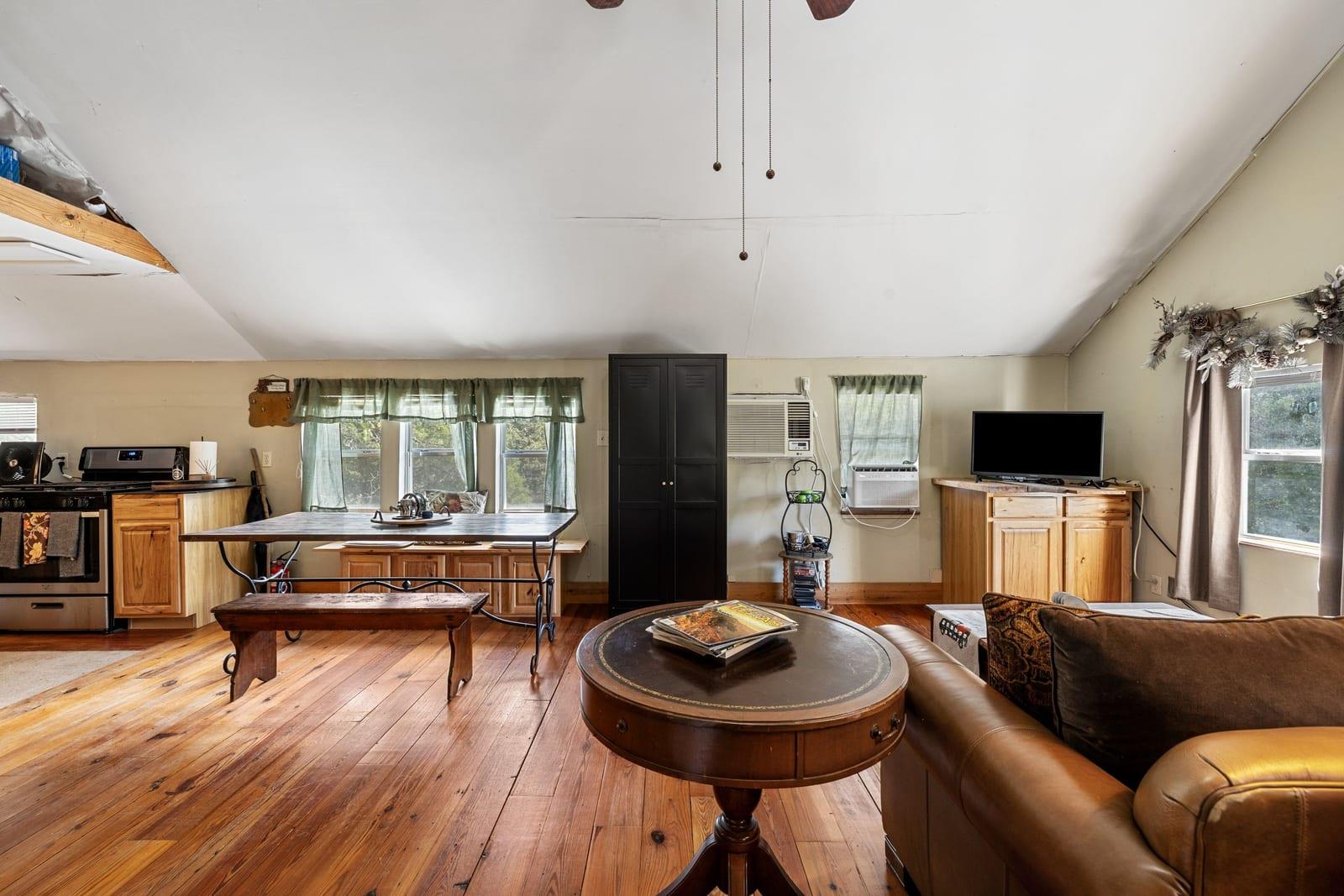 Open living room and kitchen with wood plank floors, a sloped ceiling, and a leather sofa.