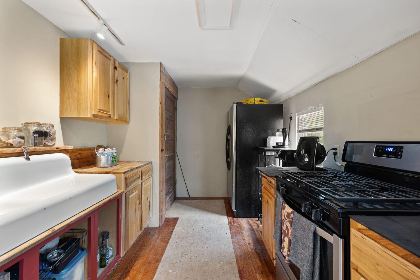 Narrow kitchen with honey-colored wood cabinets, a farmhouse sink, and black appliances.