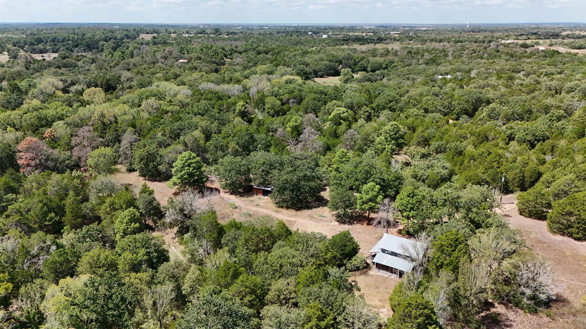 Aerial view of a wooded property with a house, outbuilding, and dirt clearings.