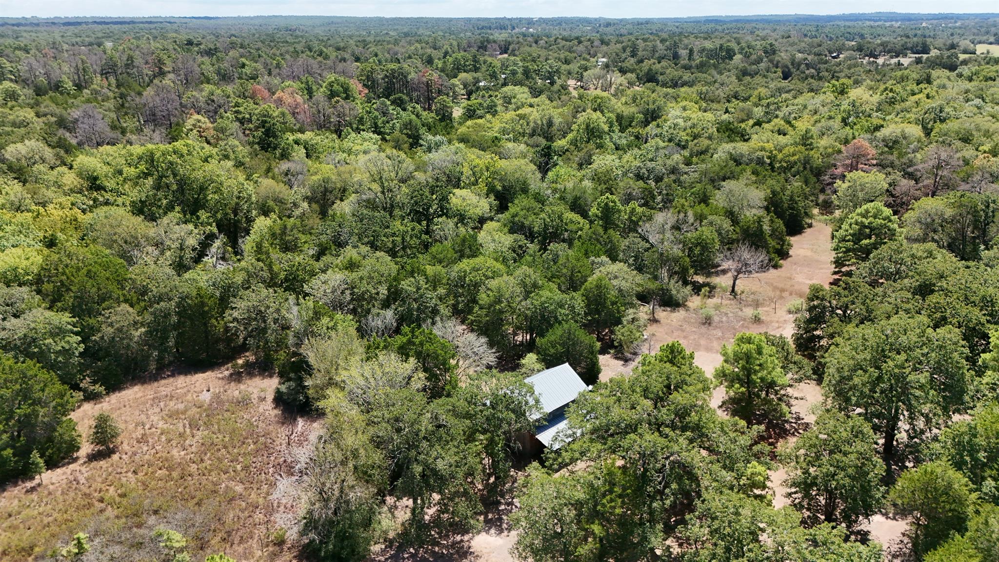 Aerial view of wooded property with open clearings and a small metal-roofed building.