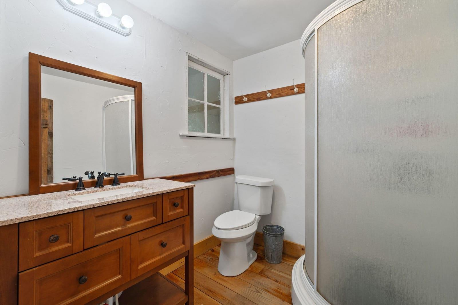 Bathroom with a wood vanity, framed mirror, curved shower enclosure, and wood plank flooring.