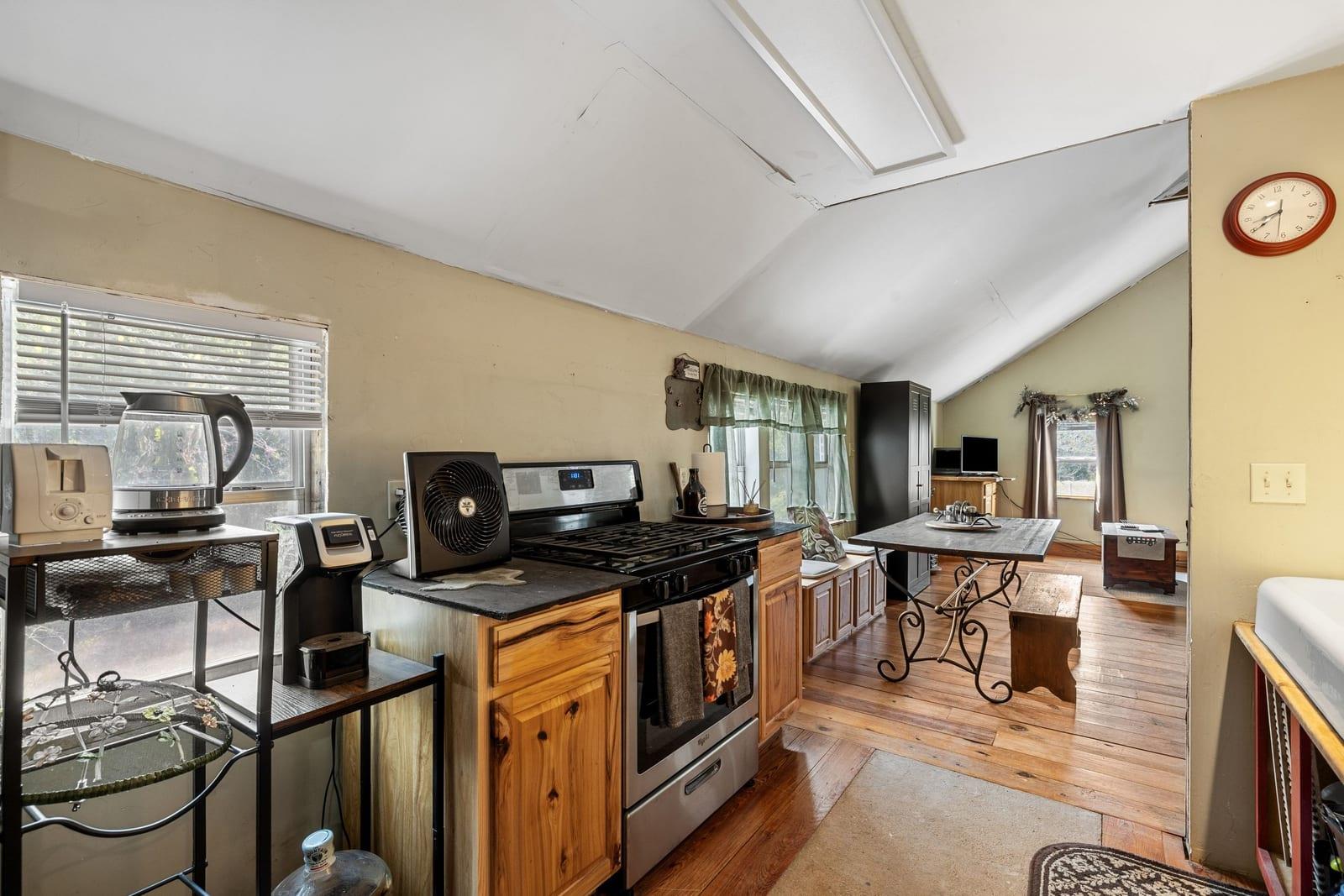 Kitchen and dining area with wood floors, a black range, wooden cabinets, and a visibly damaged sloped ceiling.