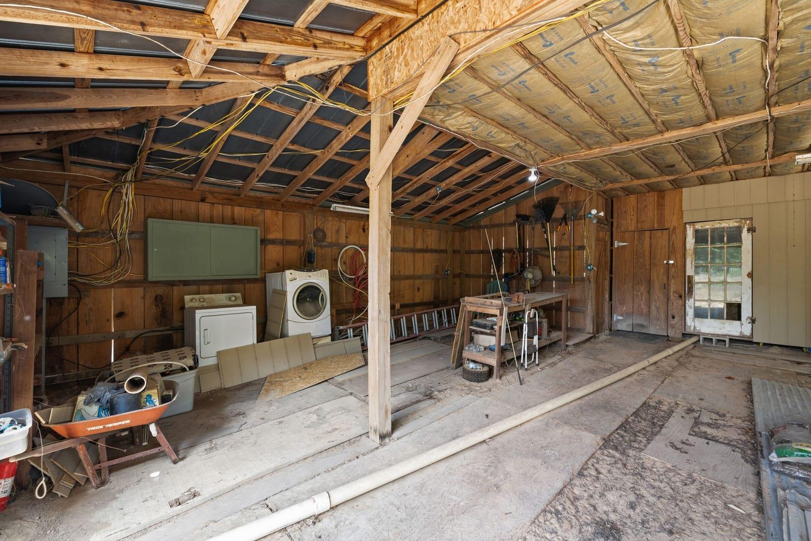 Unfinished garage workshop with exposed roof framing, washer and dryer, tools, and a pipe across the floor.