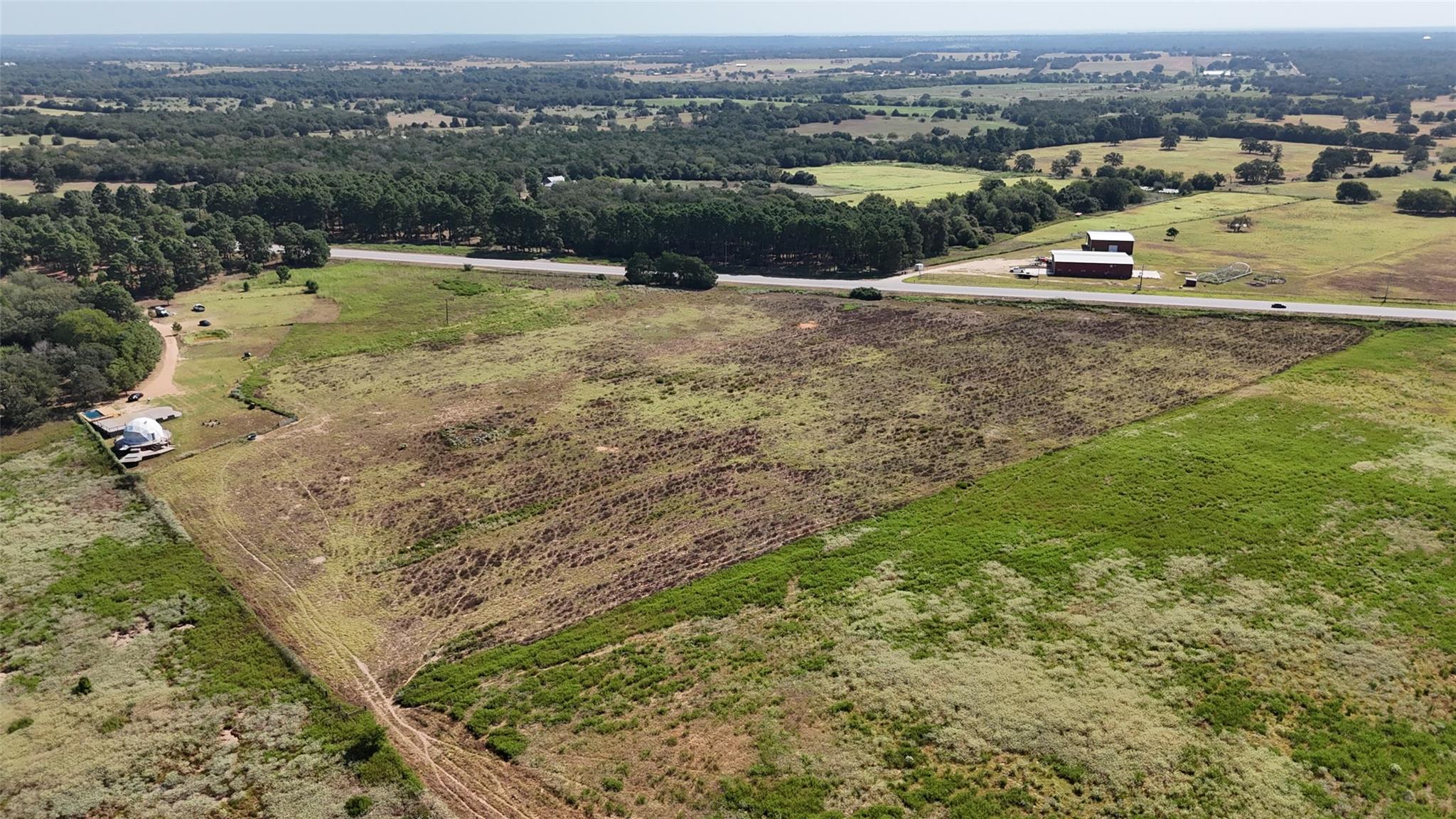 Aerial view of rural land with a highway, scattered trees, and a small pool near the left edge.