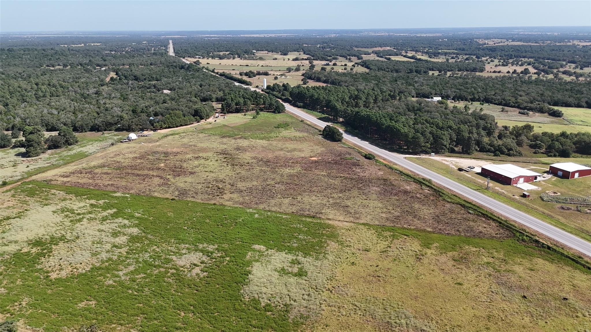 Aerial view of open grassy acreage beside SH 304, with wooded countryside beyond.