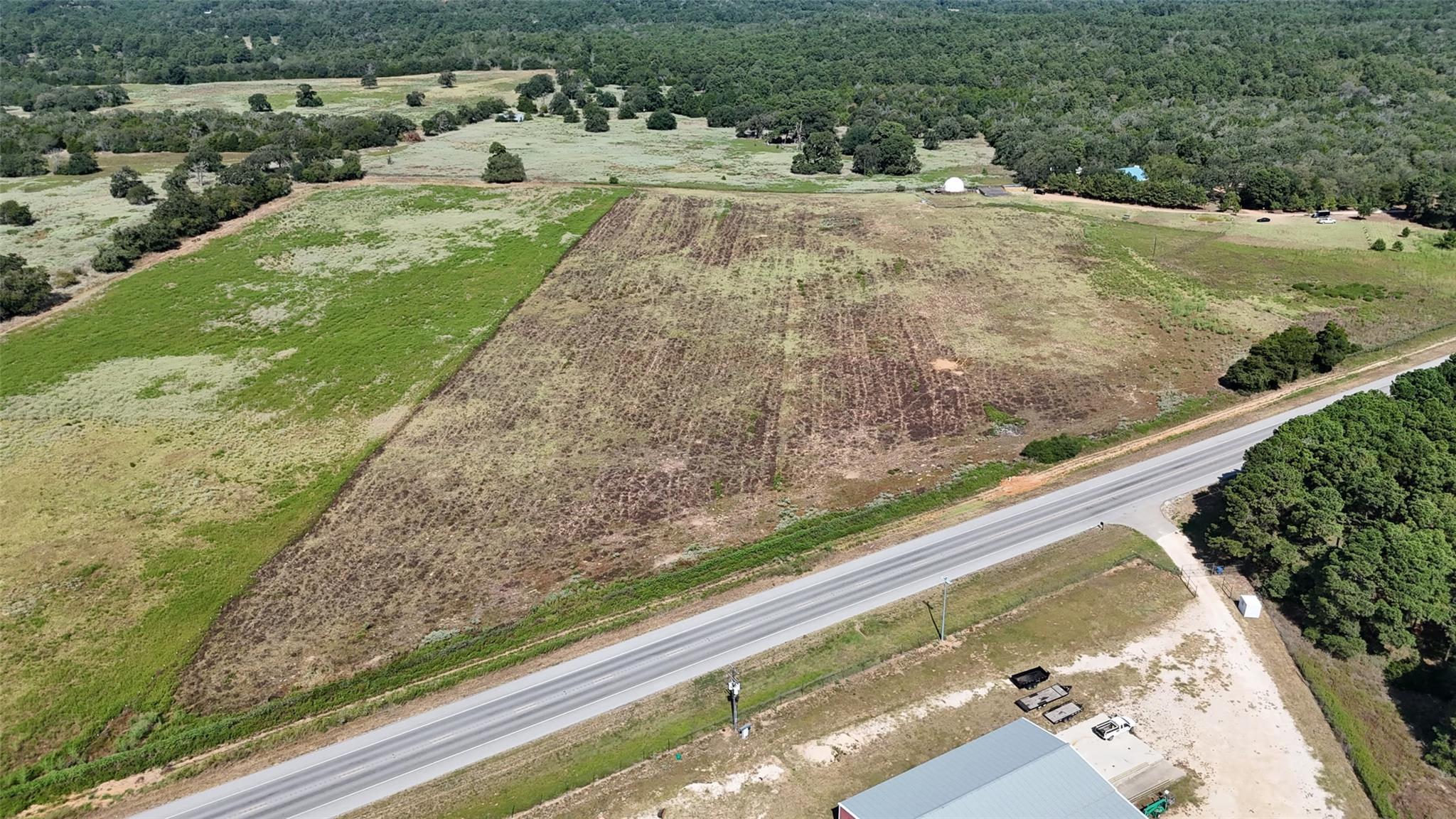 Aerial view of open fields and wooded acreage beside a highway.