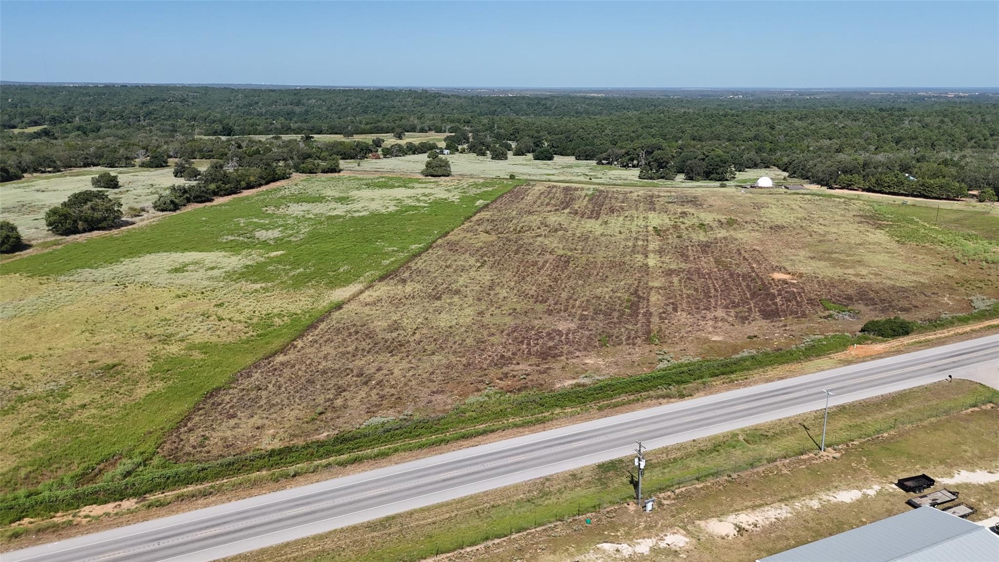 Aerial view of open fields and woodland beside a paved highway.