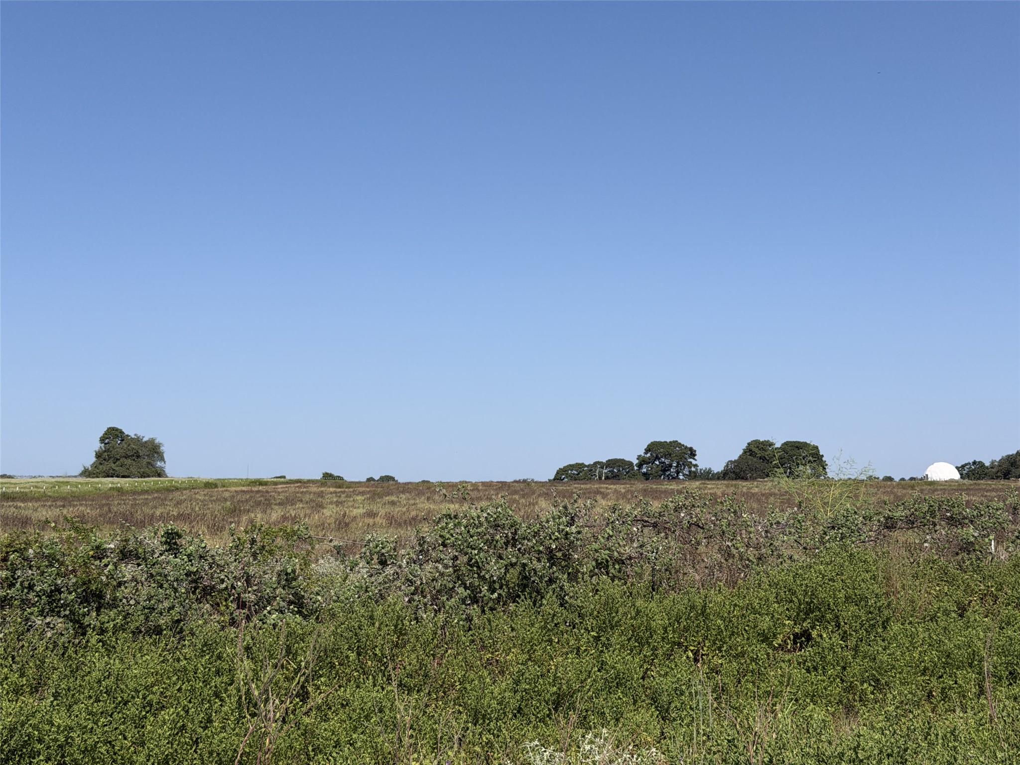 Open rural land with brush, grassy fields, scattered trees, and a small white dome in the distance.